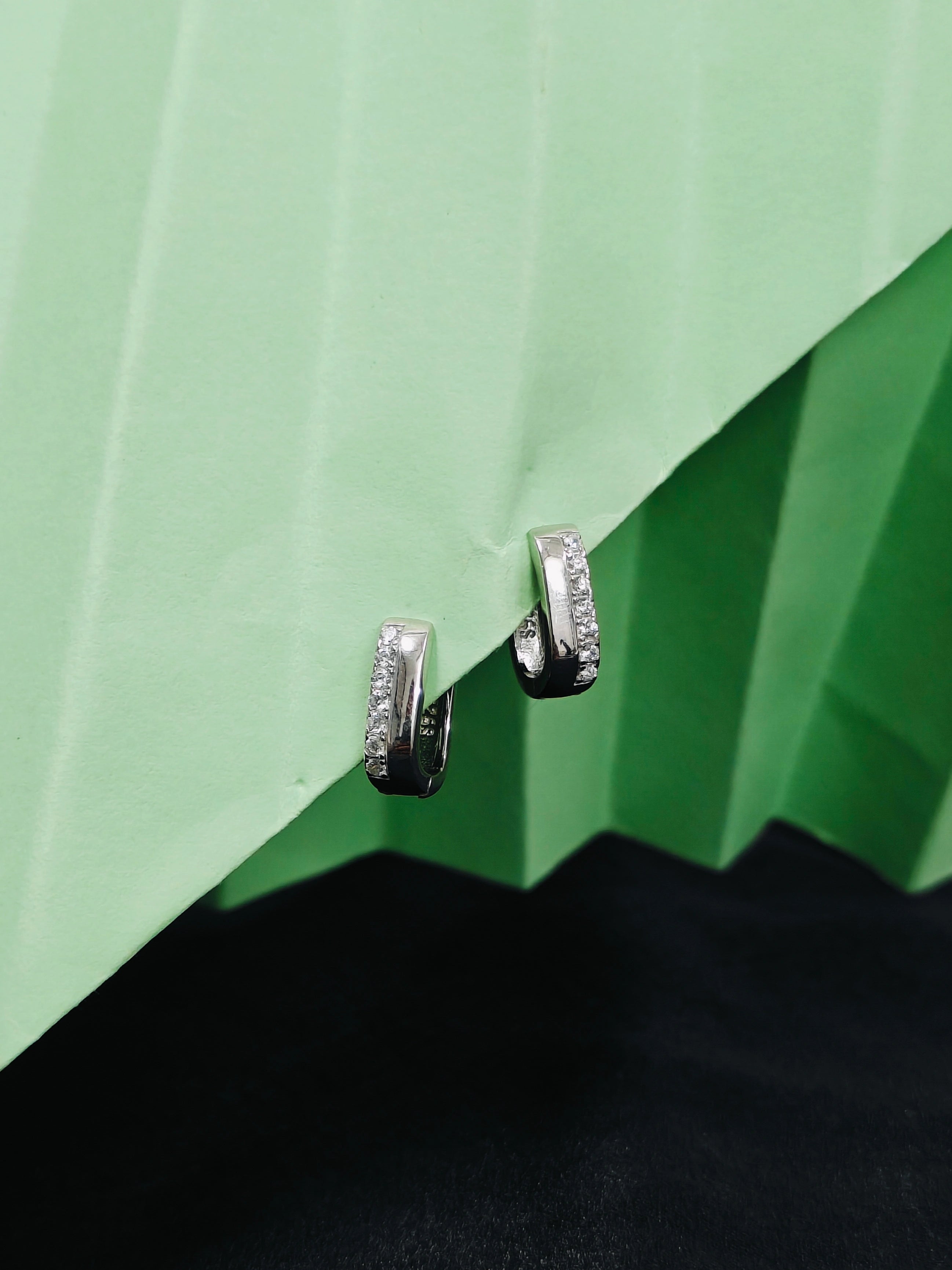 Silver hoop earrings with embedded stones on a green and black background