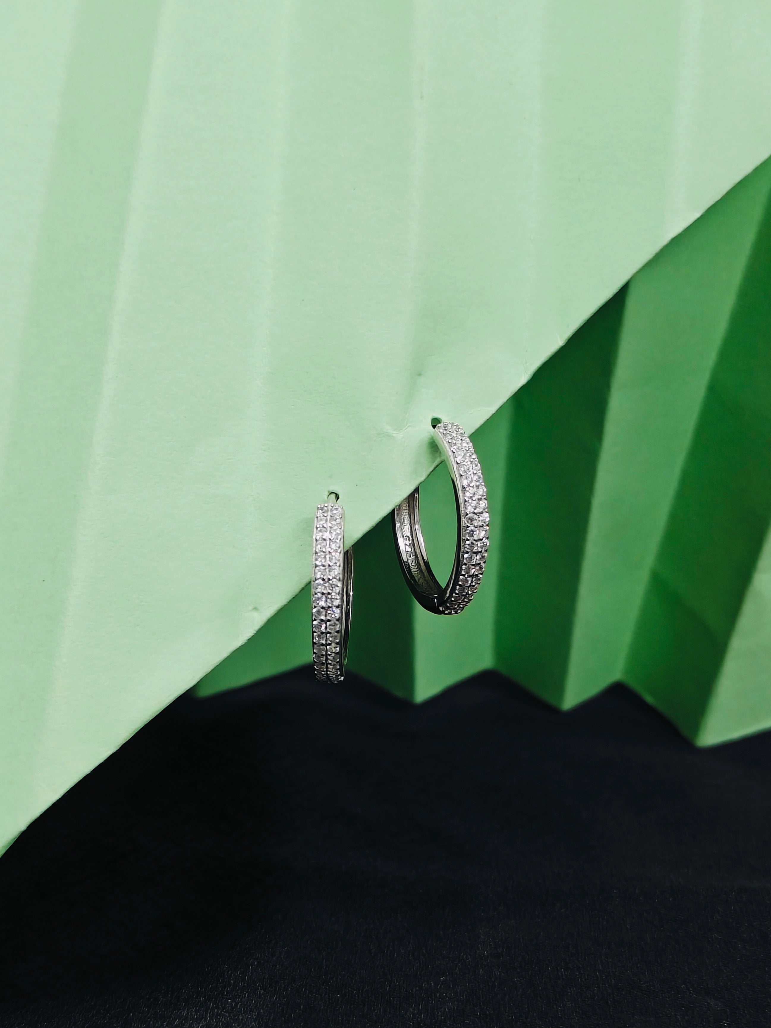 Pair of silver hoop earrings on a green and black geometric background