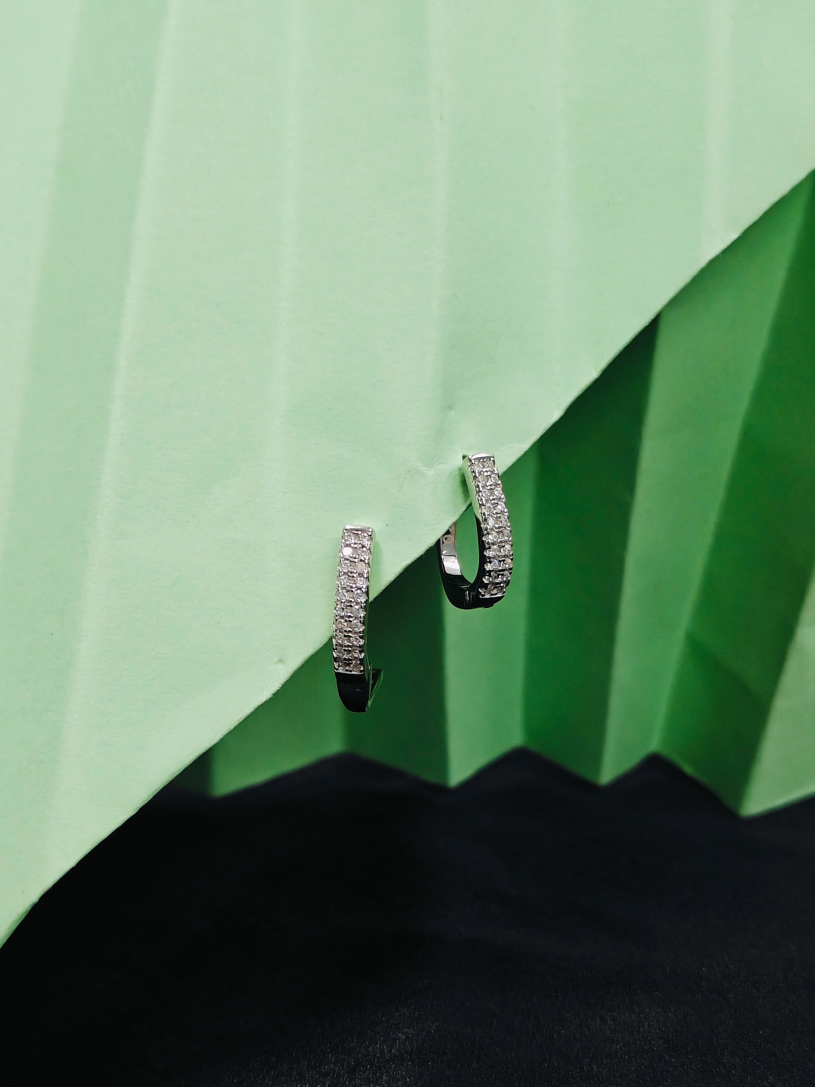 Pair of silver hoop earrings on a green textured surface
