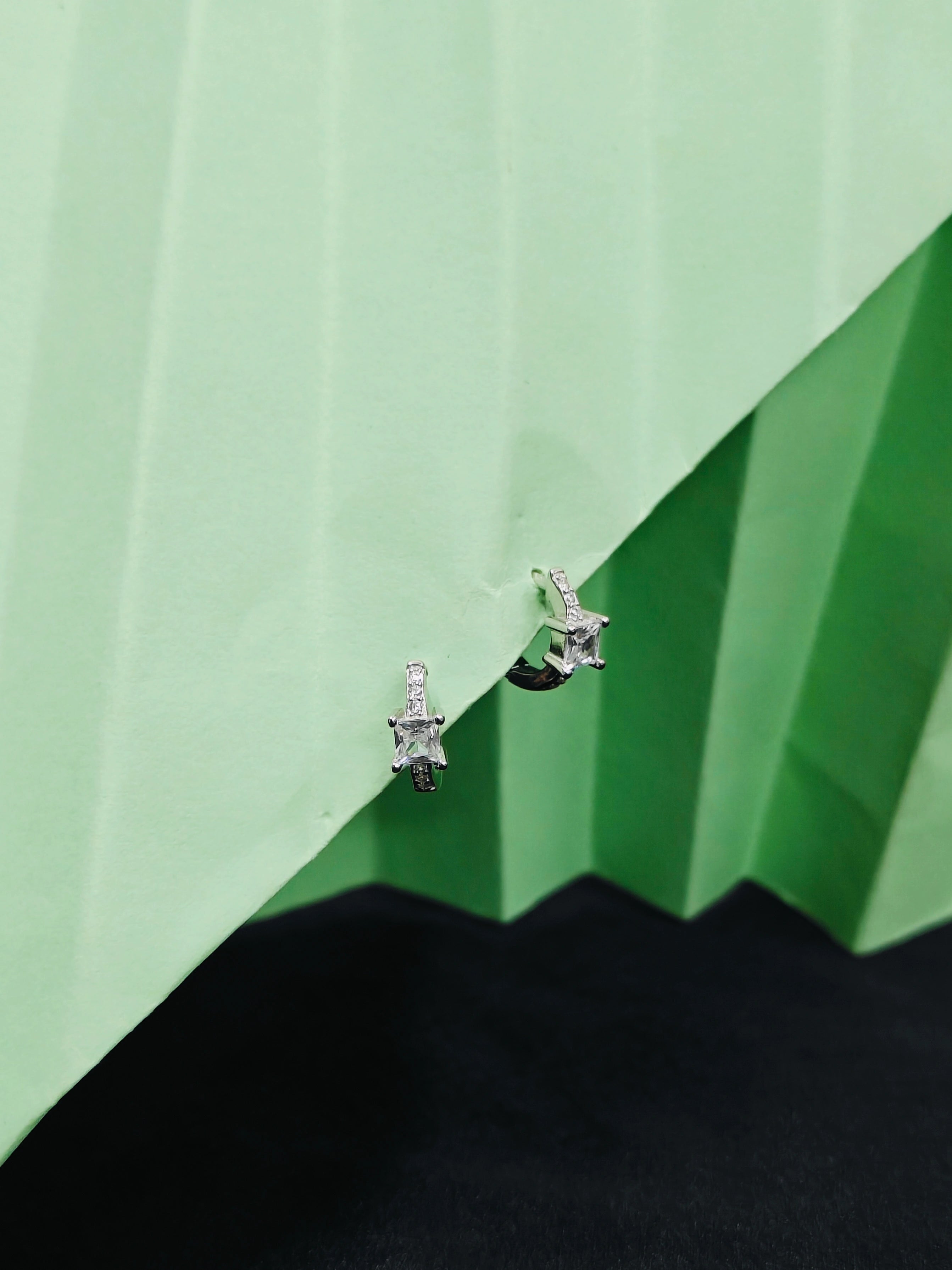 Pair of silver earrings with gemstones on a green and black geometric background