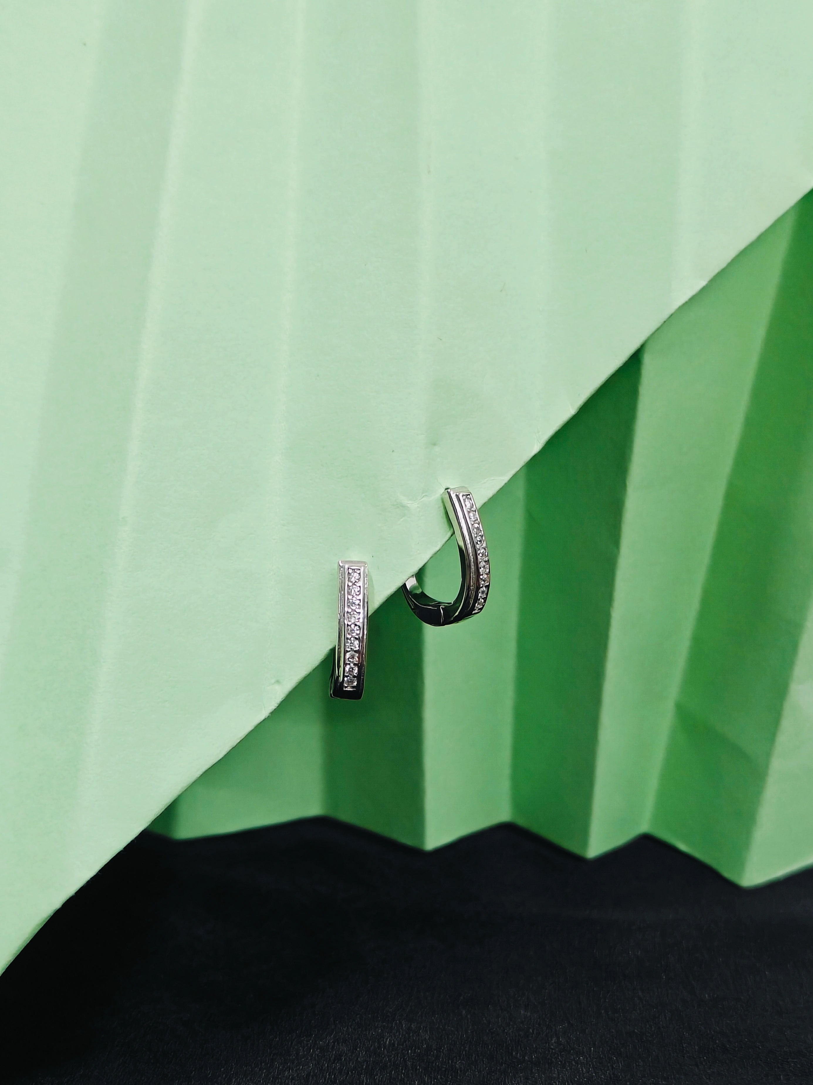 Silver hoop earrings with black accents on a green textured surface