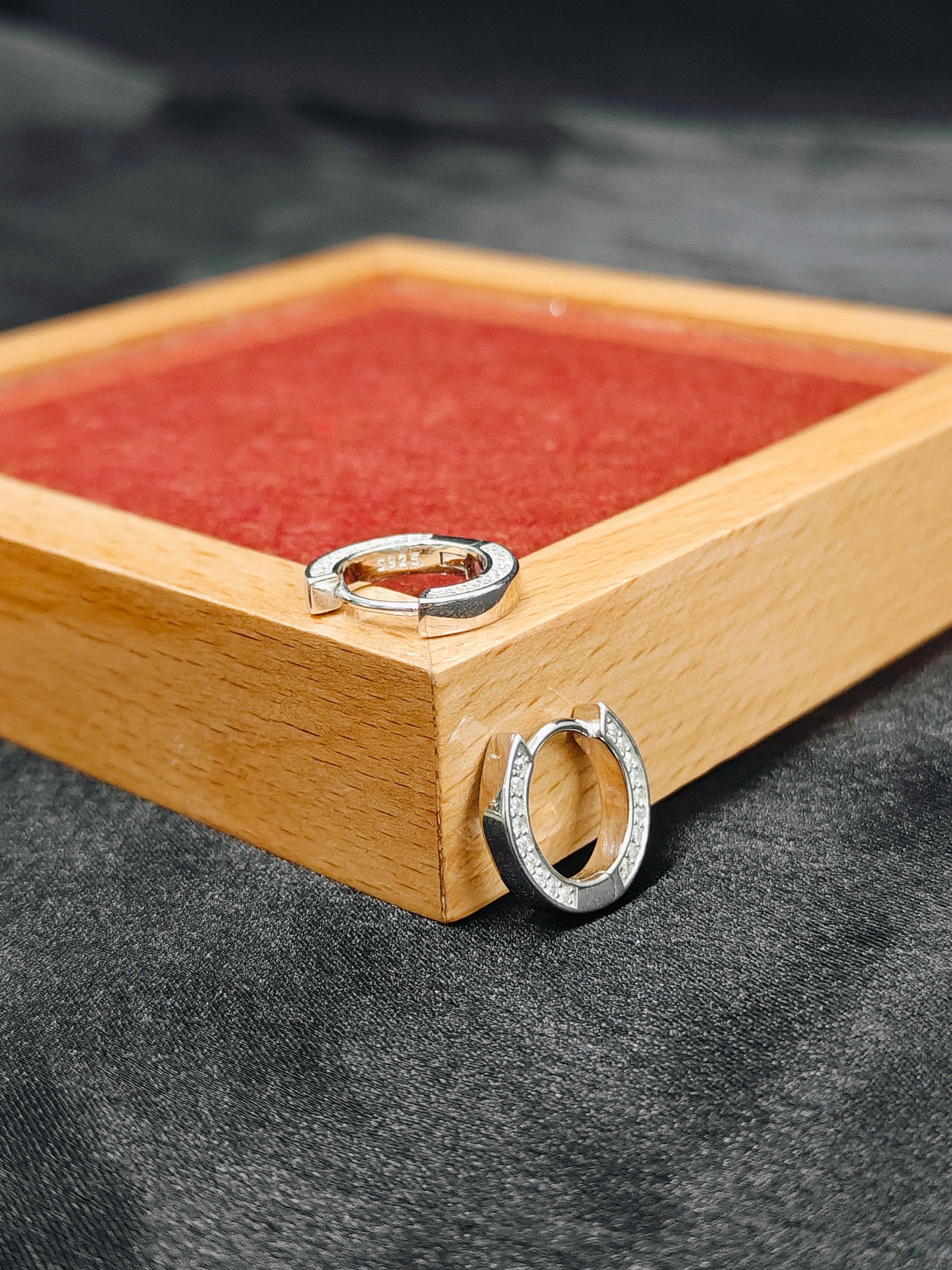 Two silver hoop earrings on a wooden tray with a red interior.