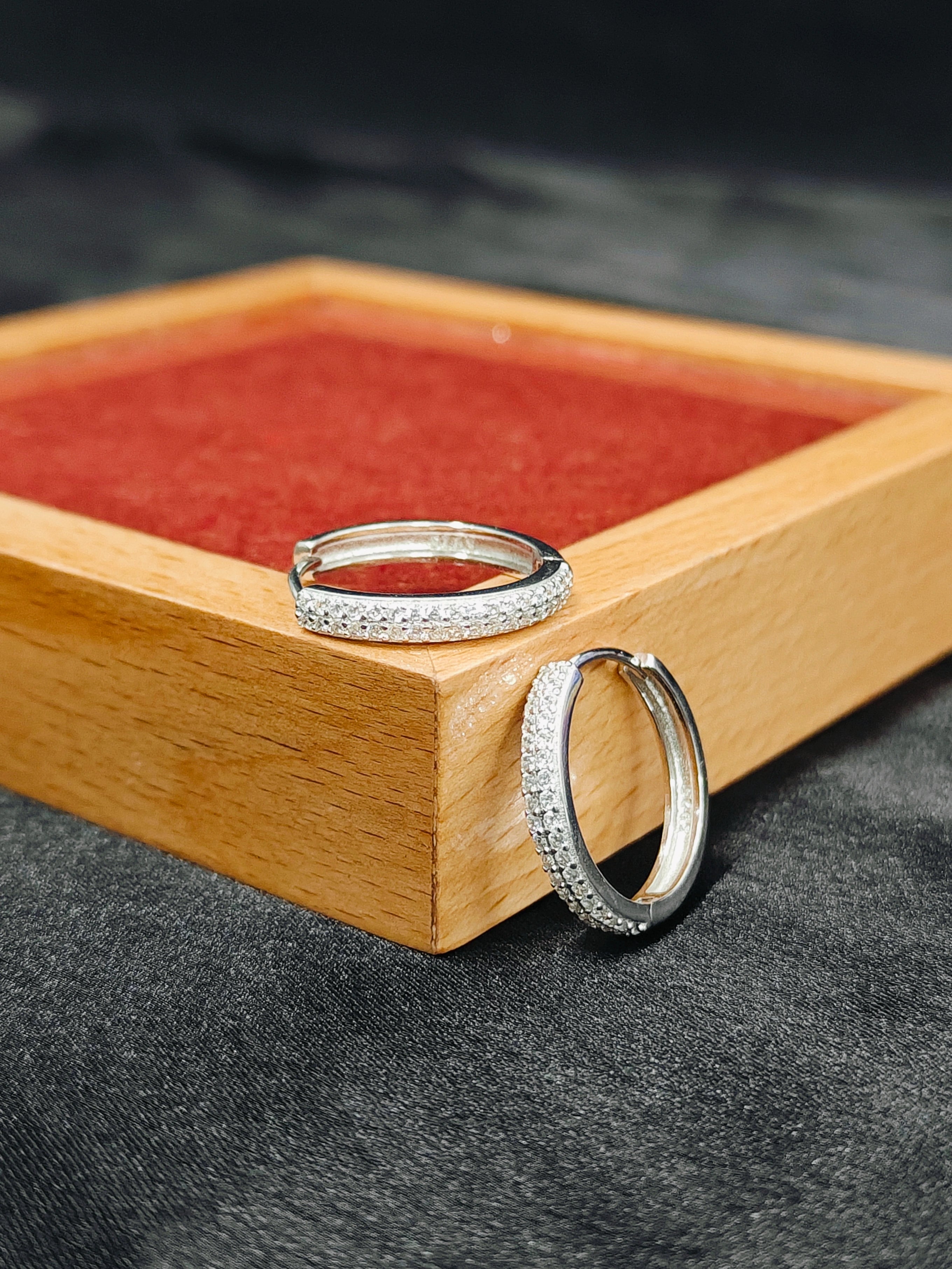 Two silver rings on a wooden tray with a red interior