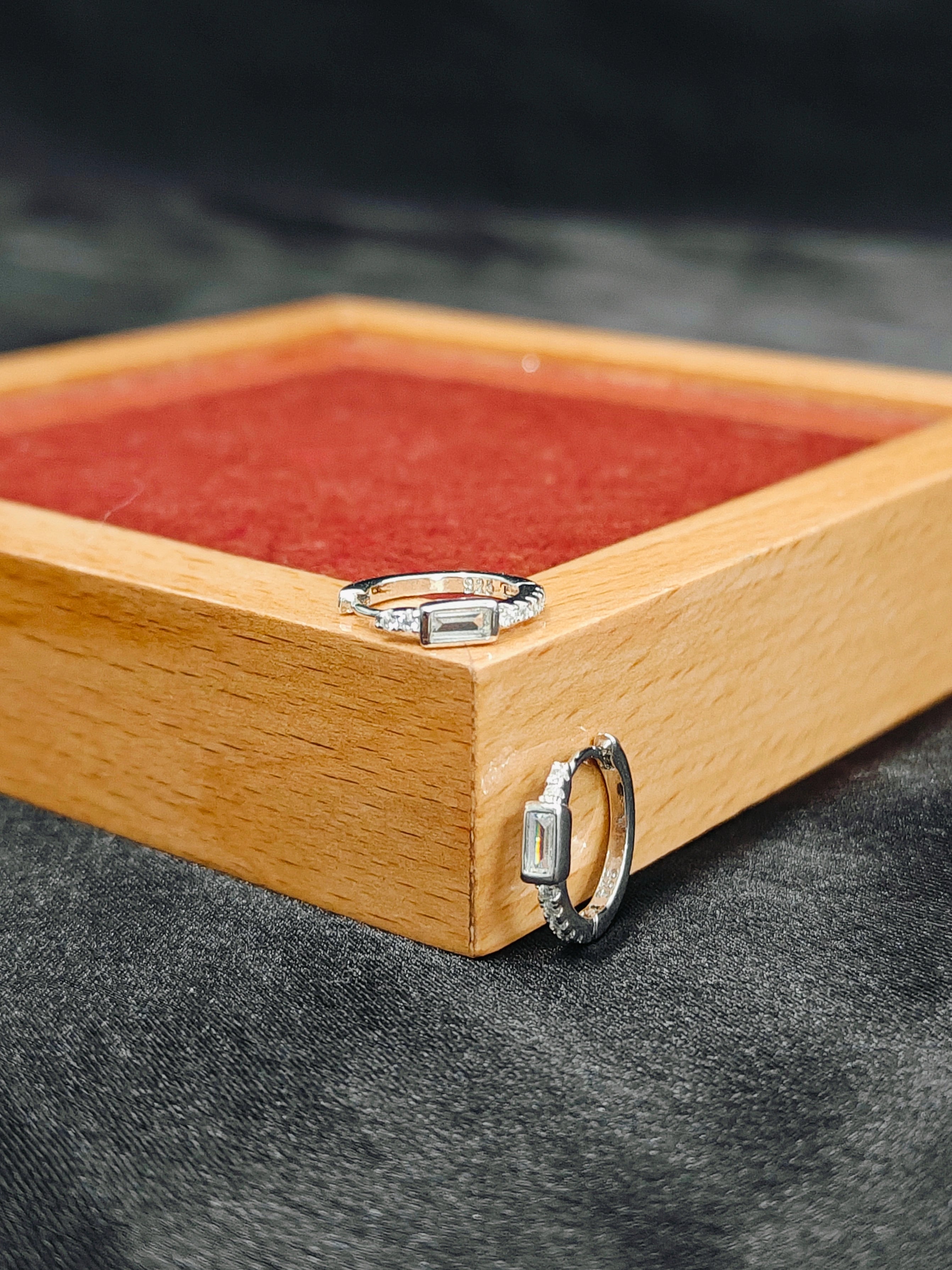 Two silver rings on a wooden box with a red interior.