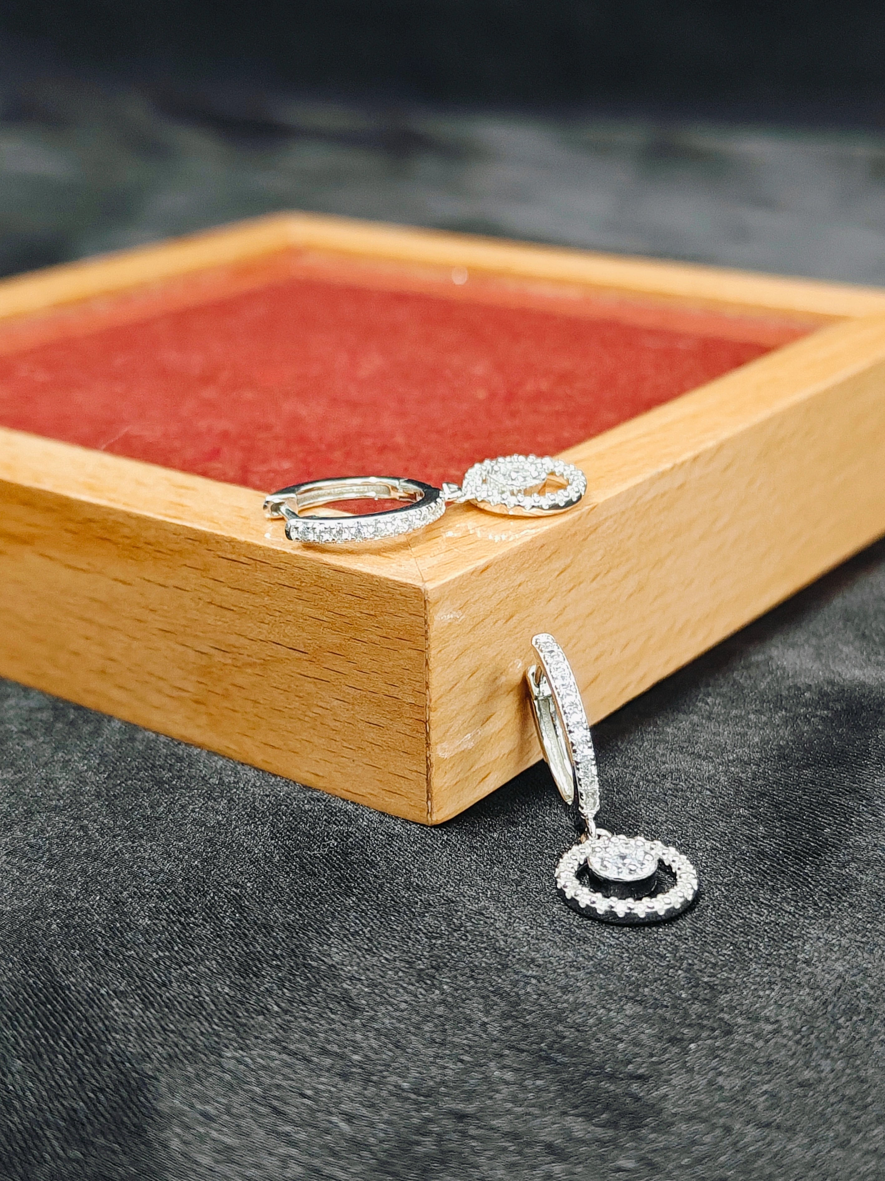 Silver hoop earrings on a wooden jewelry box with a dark fabric background