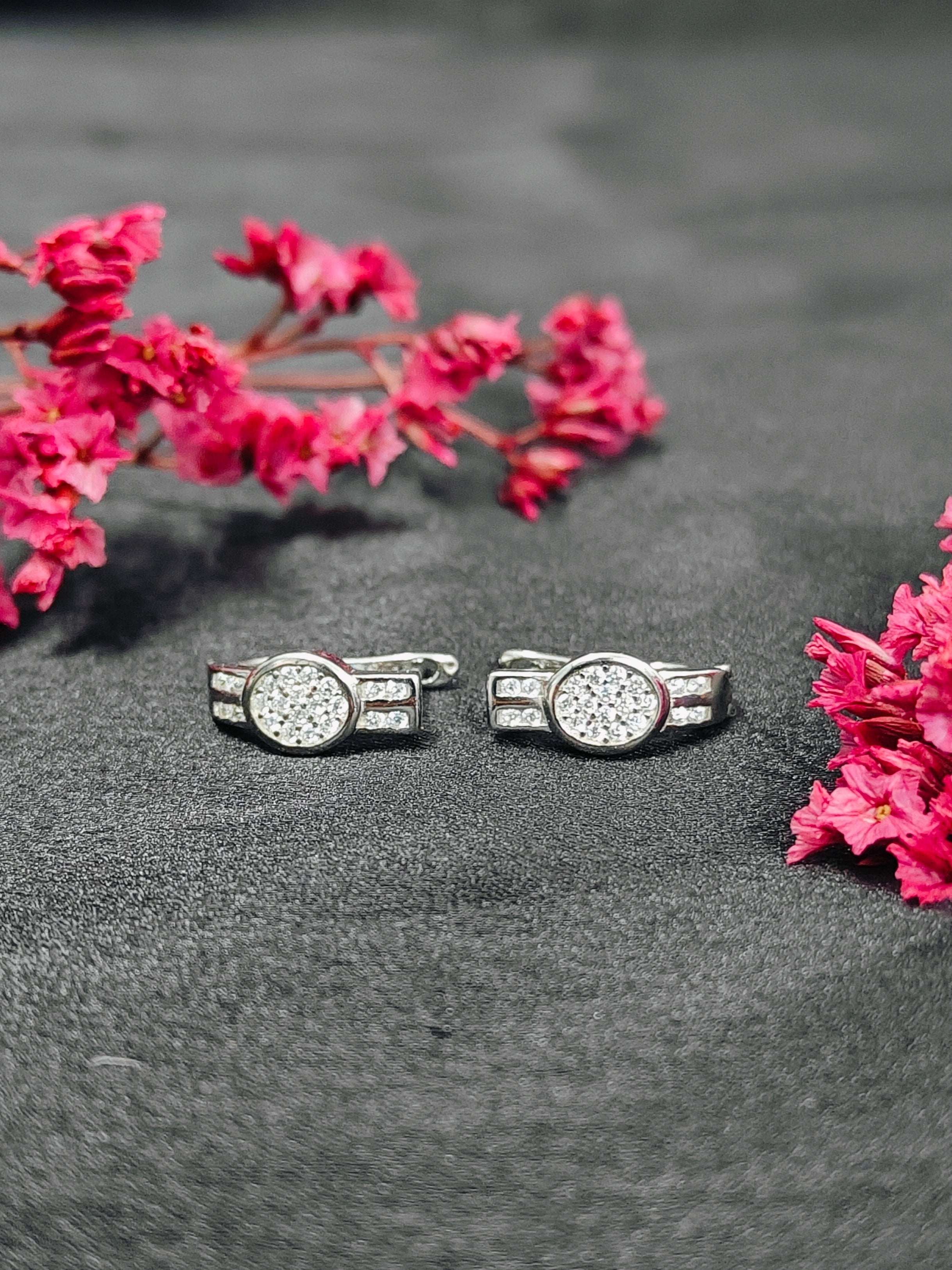 Silver cufflinks with gemstones on a dark surface with pink flowers