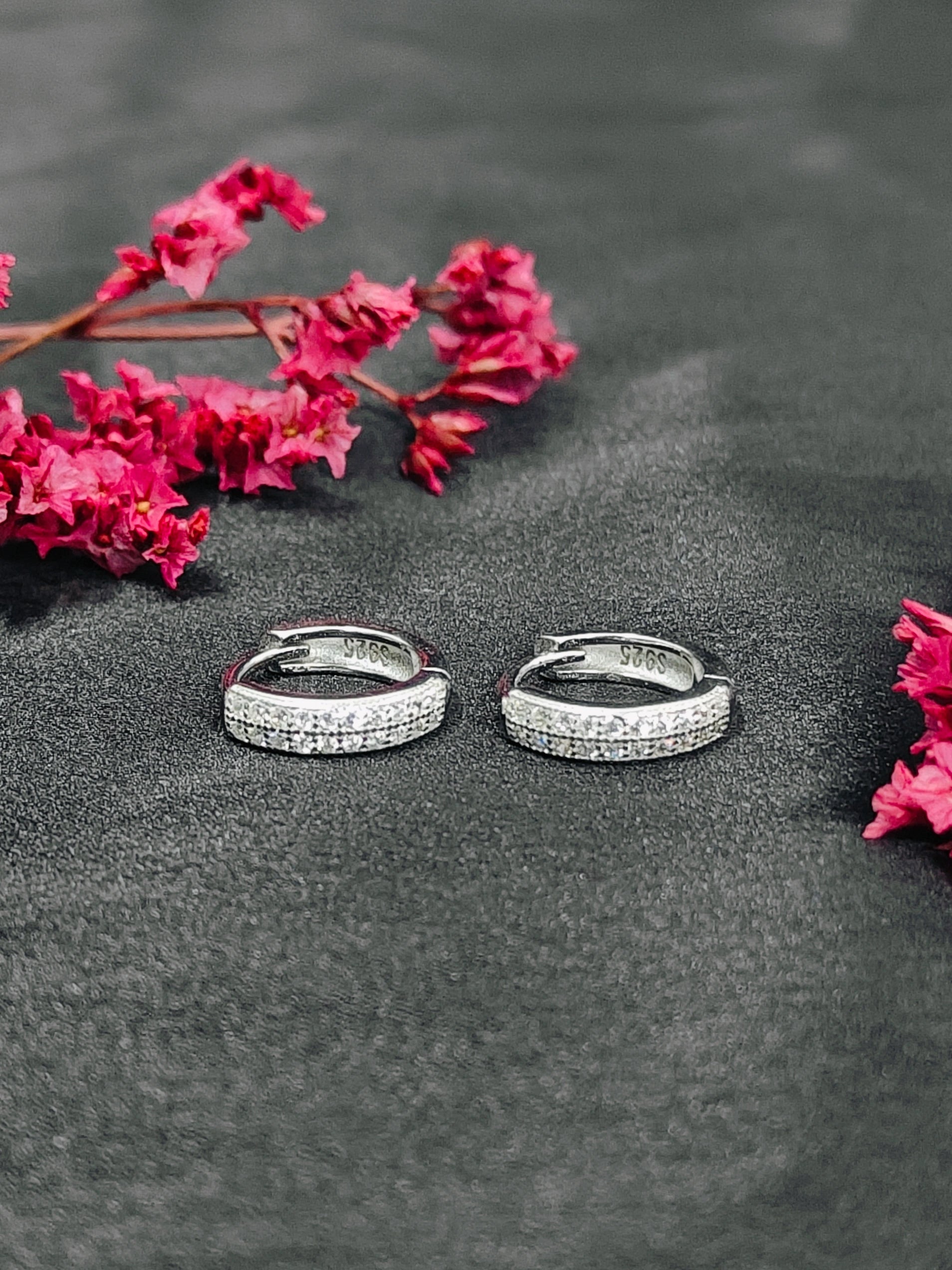 Silver hoop earrings with pink flowers on a dark surface