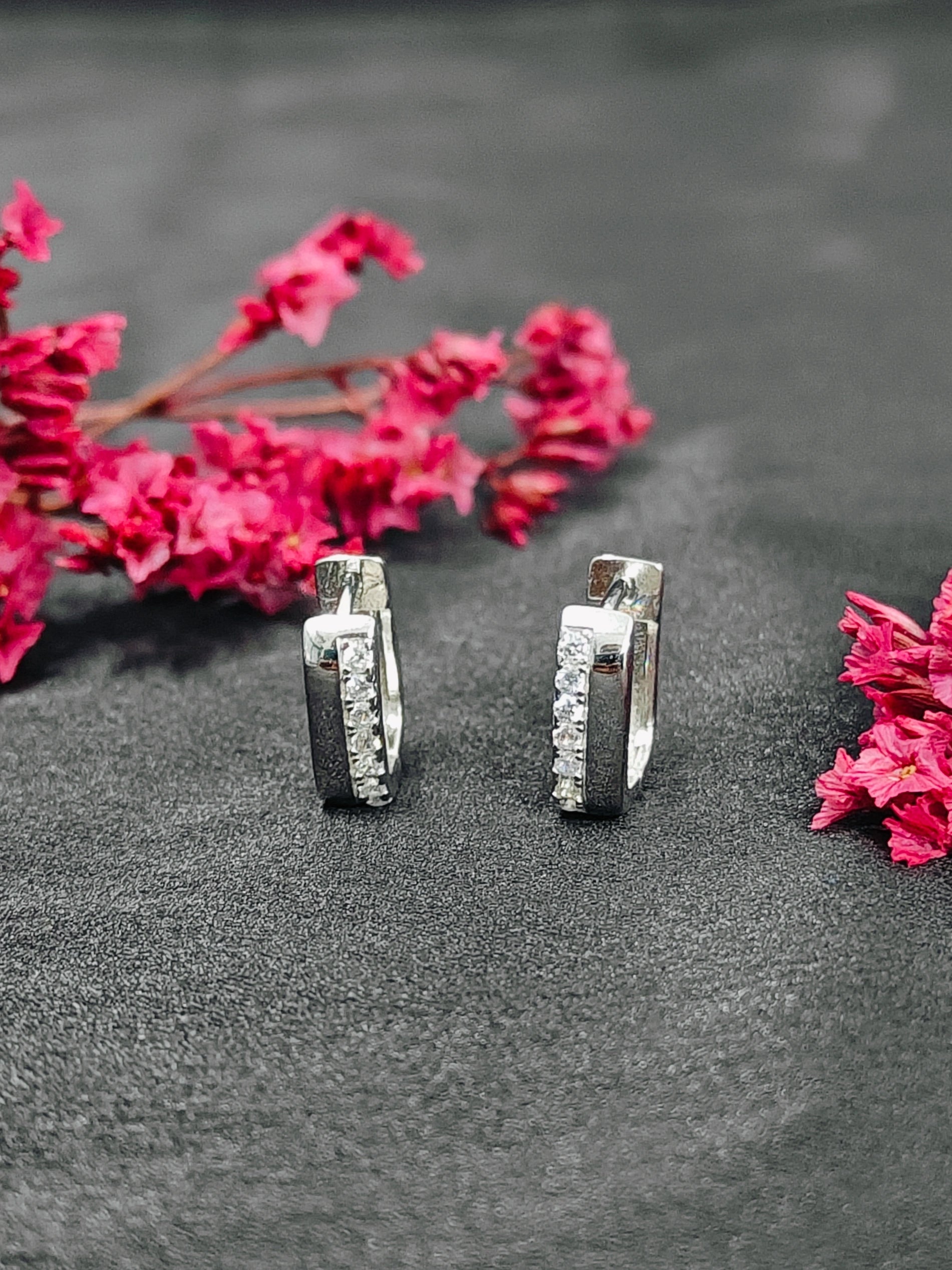 Silver hoop earrings on a dark surface with pink flowers.