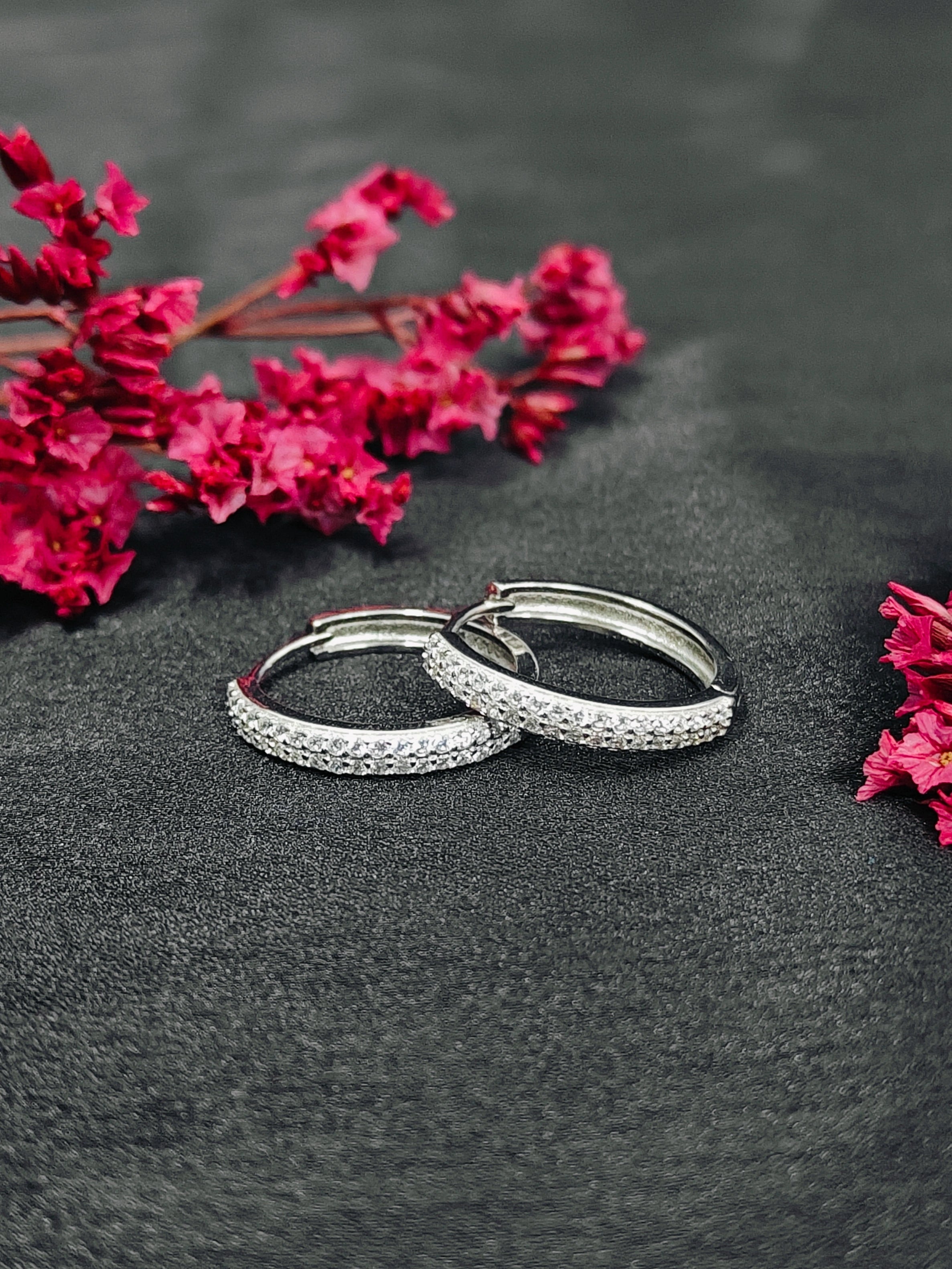 Silver hoop earrings with embedded stones on a dark surface with pink flowers.