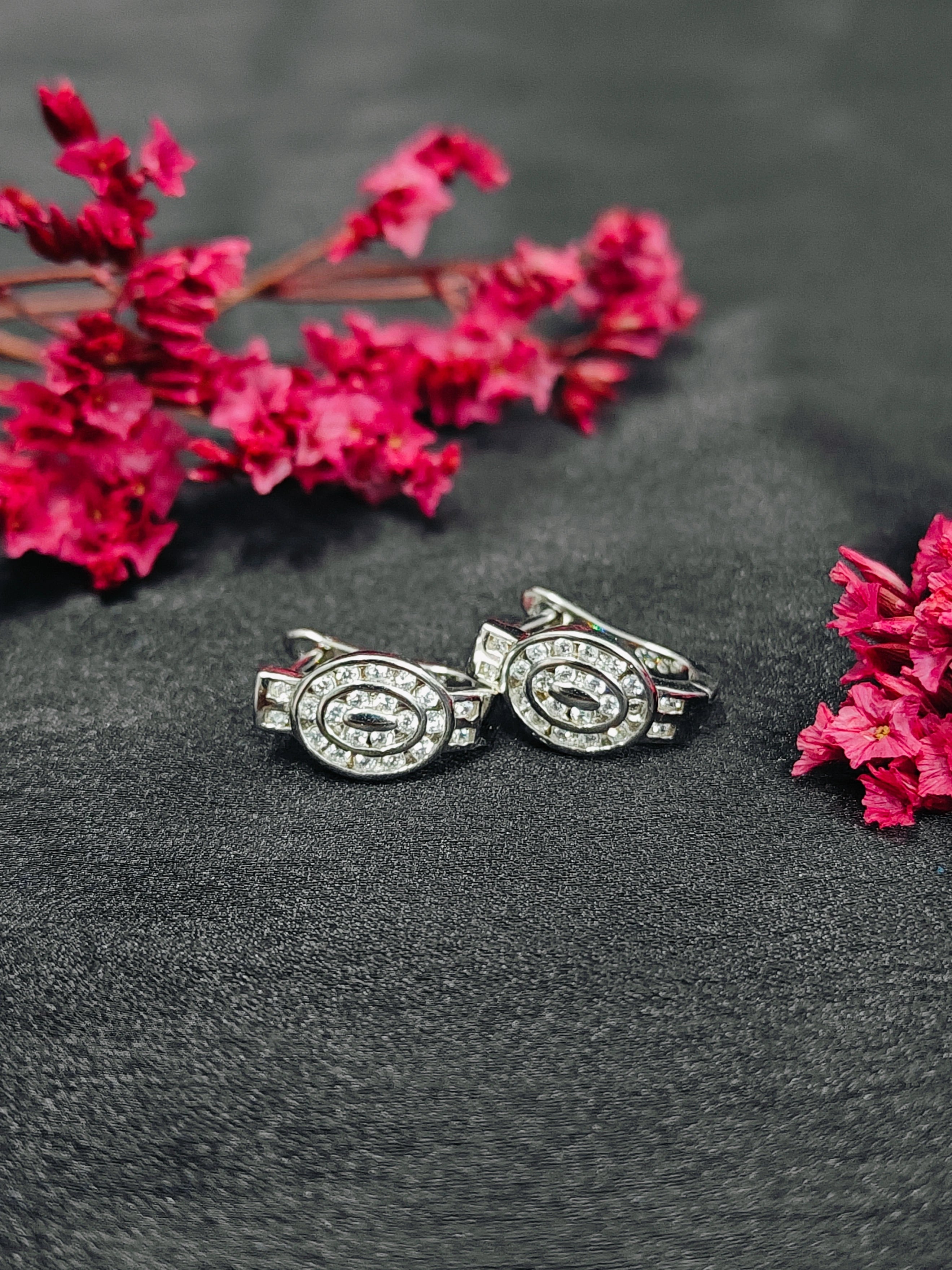 Silver earrings with gemstones on a dark surface with pink flowers