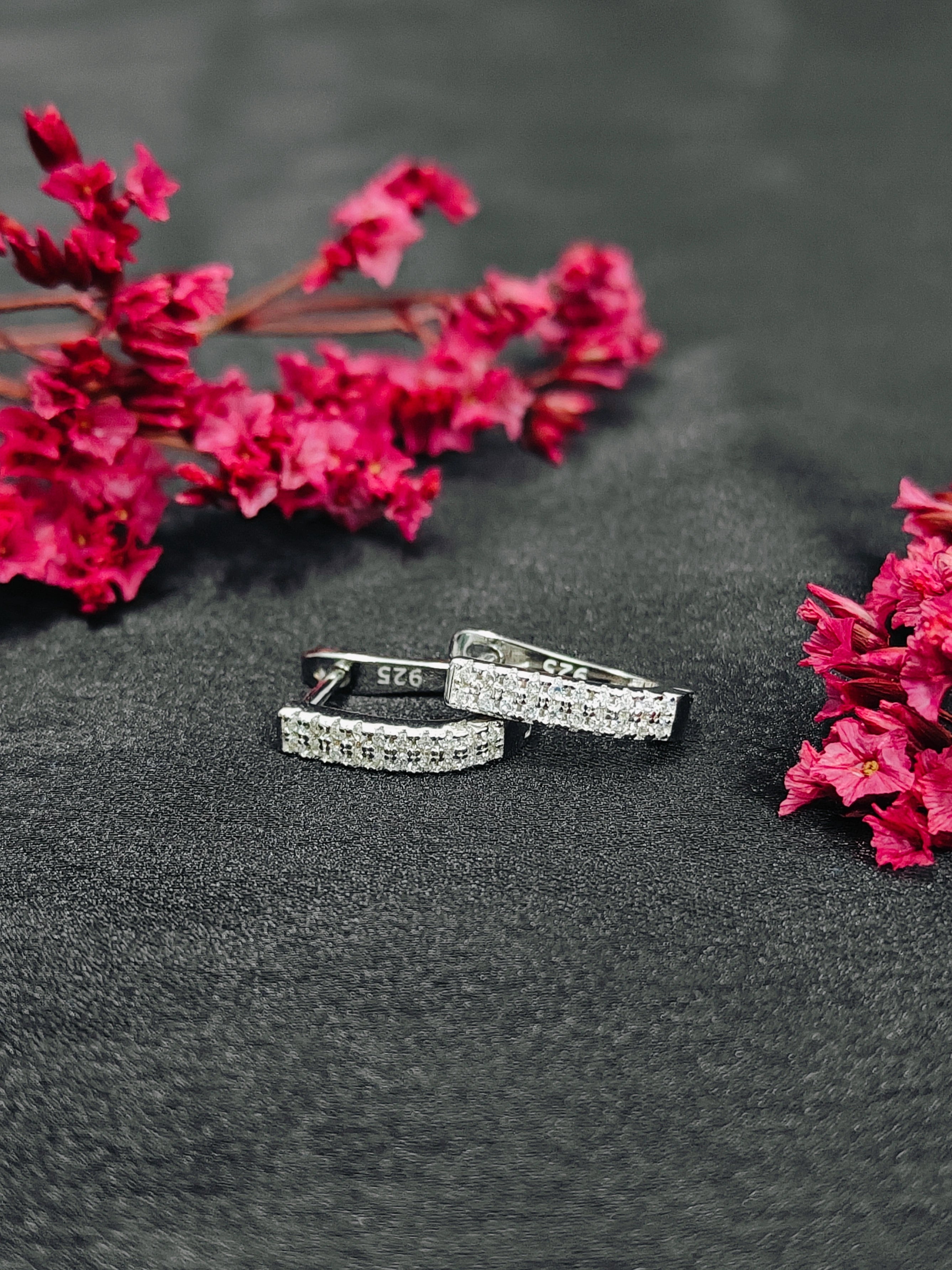 Three silver rings with gemstones on a dark surface with pink flowers.