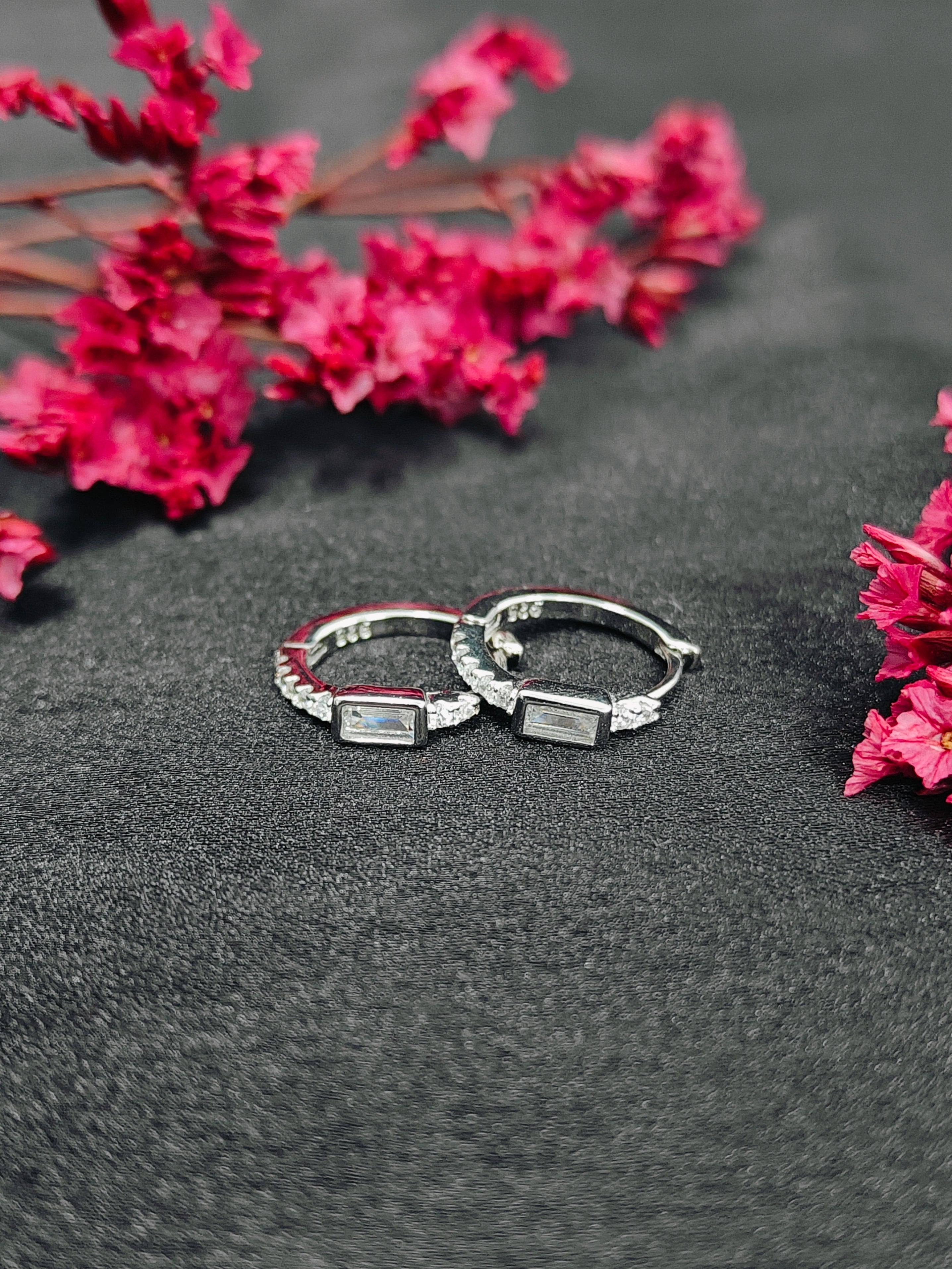 Two silver rings on a dark surface with pink flowers in the background