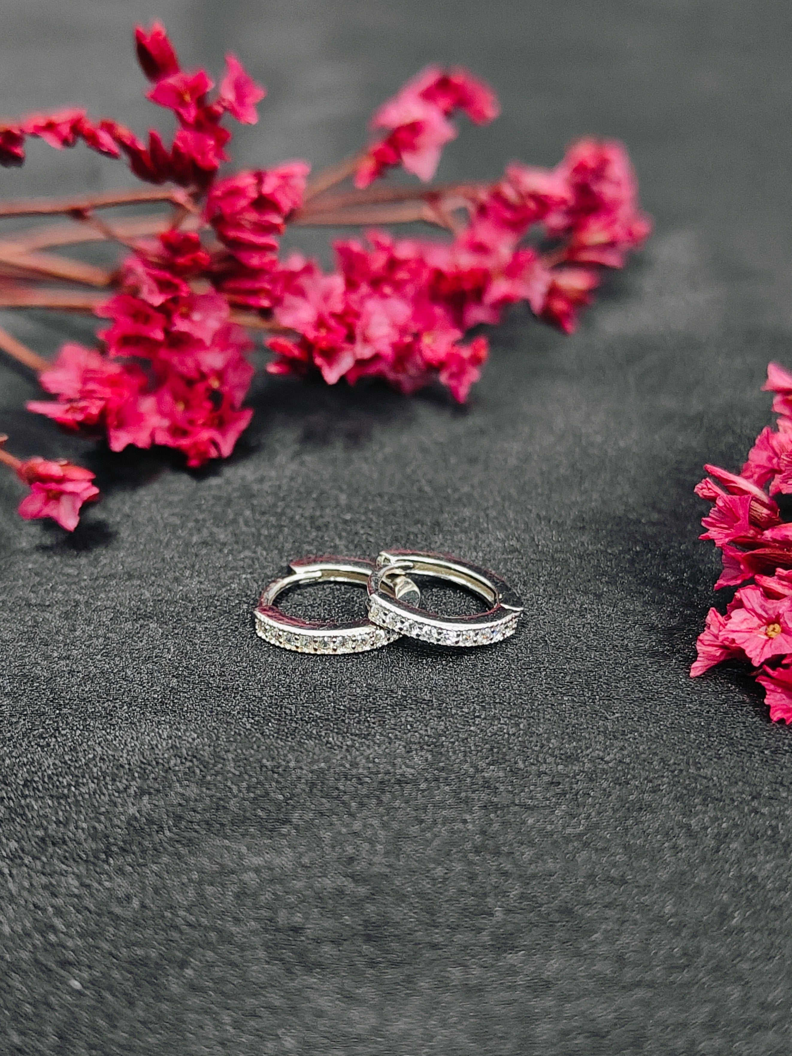 Two silver hoop earrings on a dark surface with pink flowers.