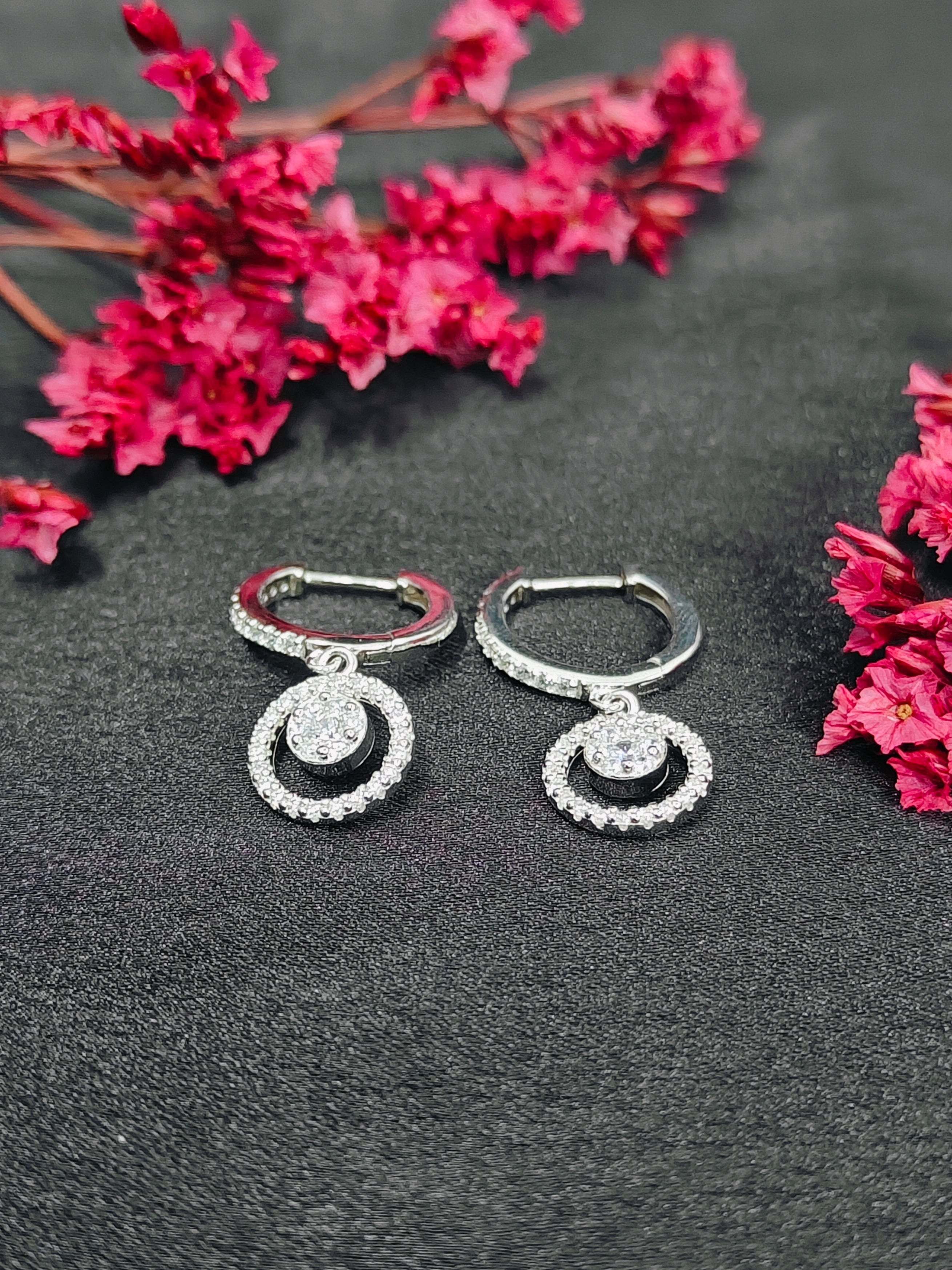 Pair of silver earrings with circular designs on a dark surface with pink flowers.