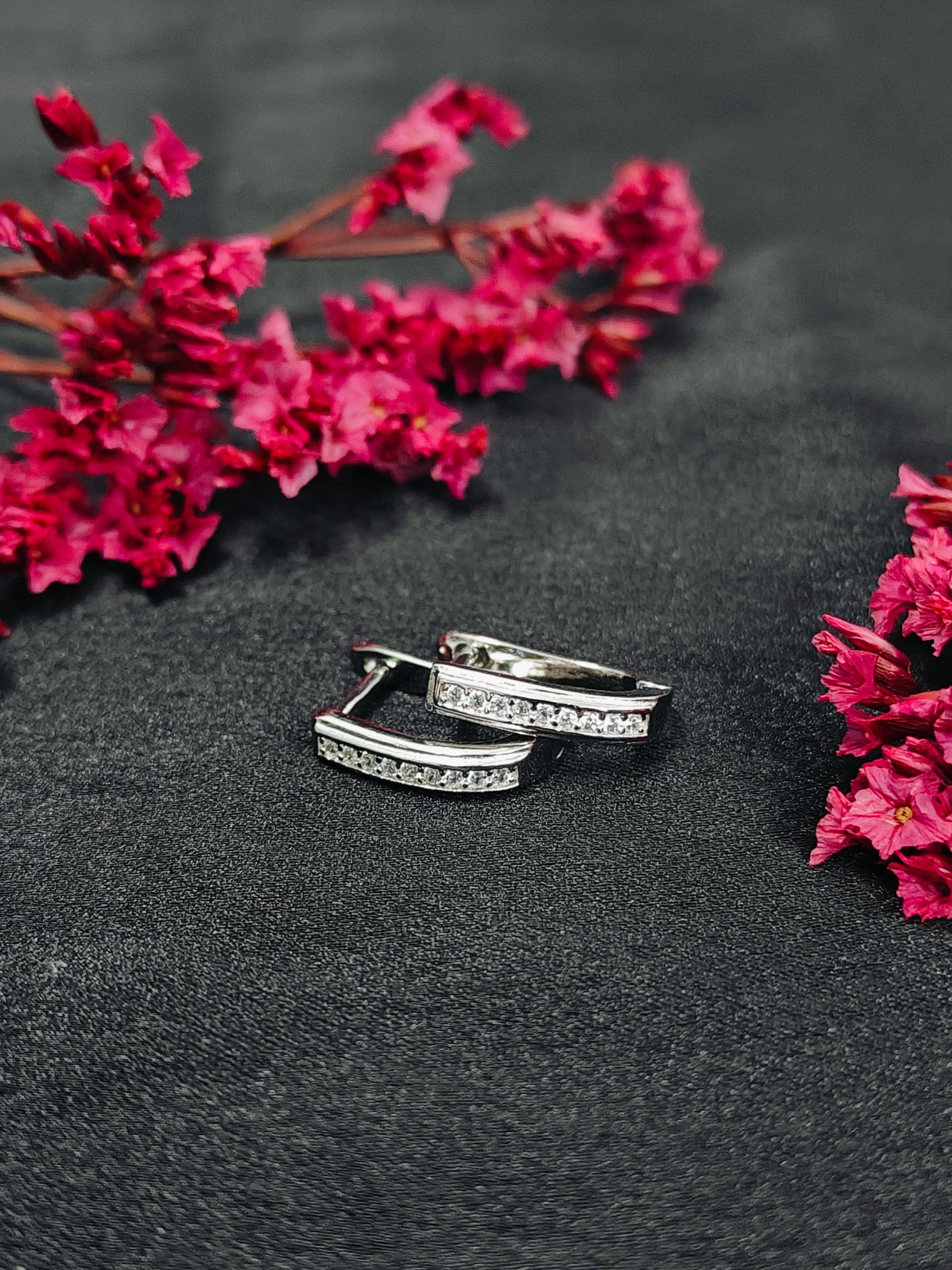 Silver hoop earrings on a dark surface with pink flowers