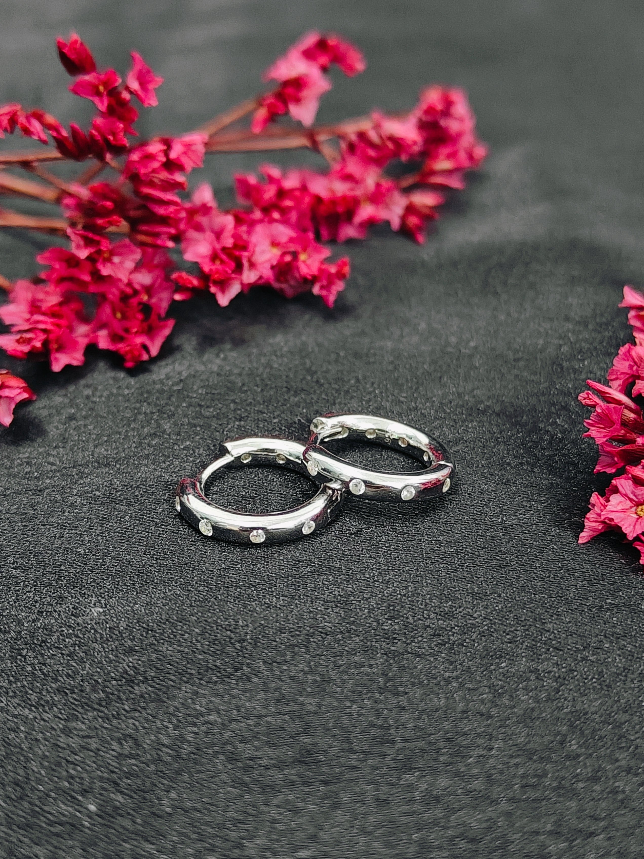 Silver hoop earrings on a dark surface with pink flowers.
