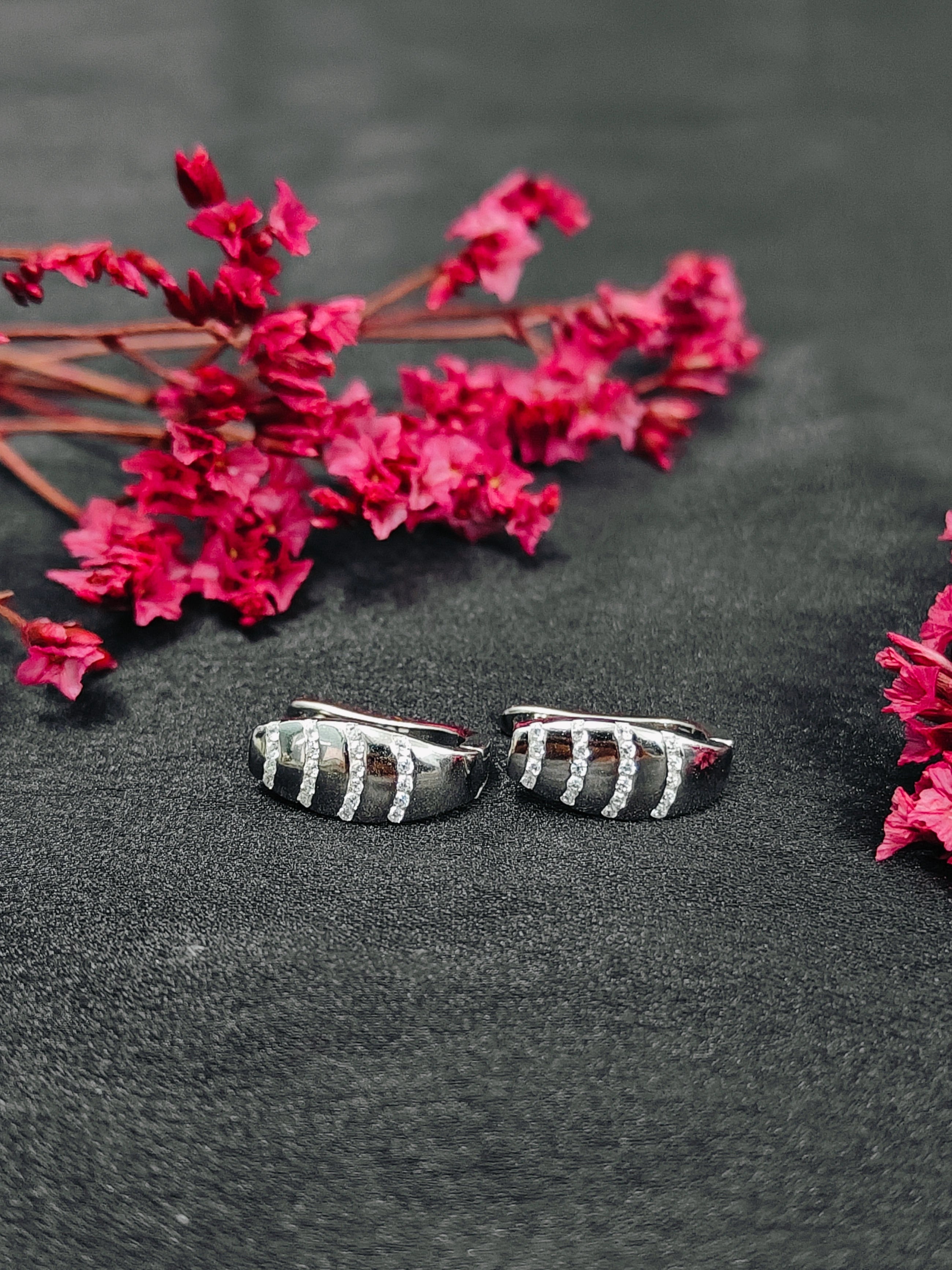 Pair of silver earrings with red flowers on a dark surface