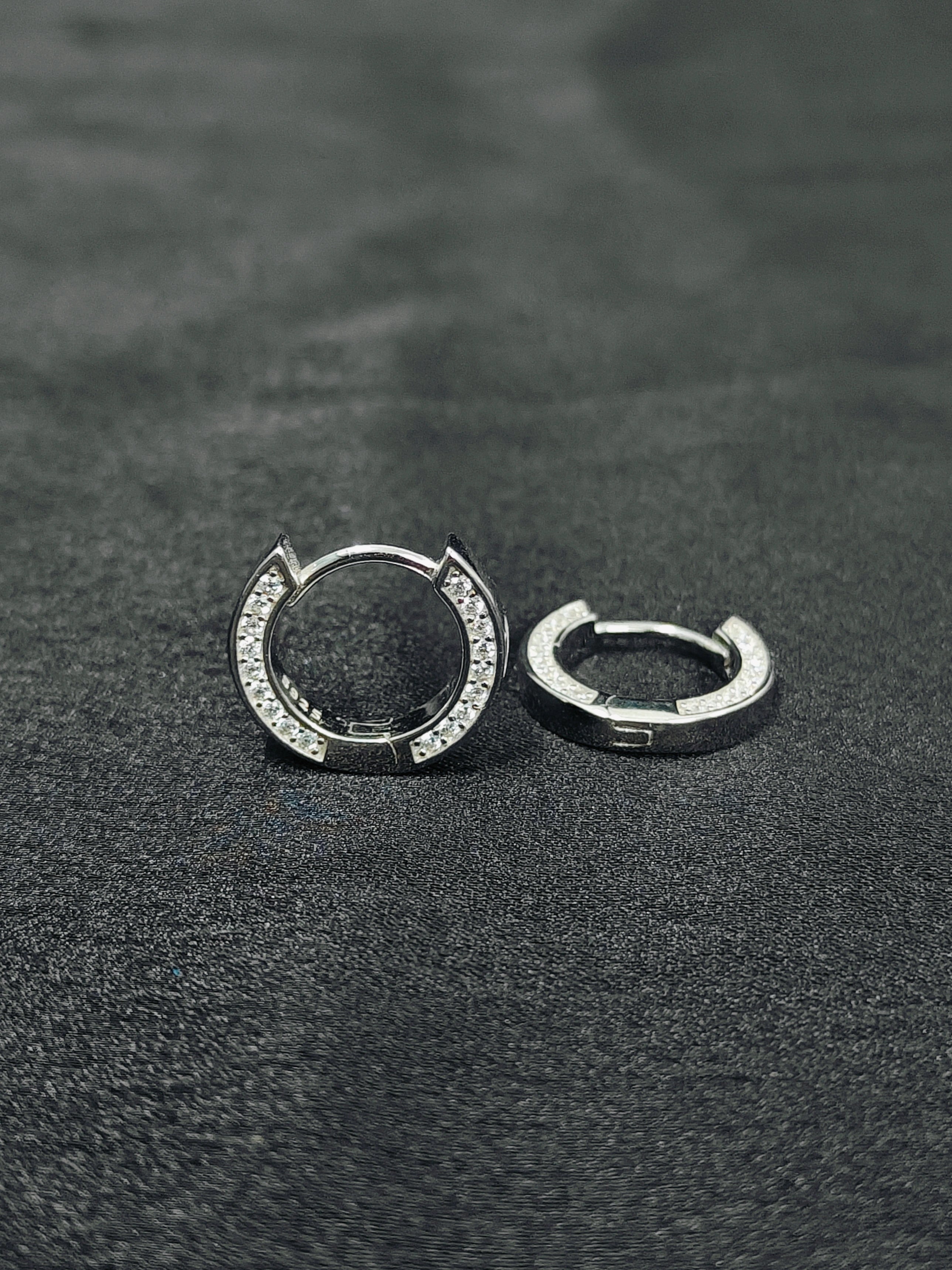 Pair of silver hoop earrings on a dark textured surface