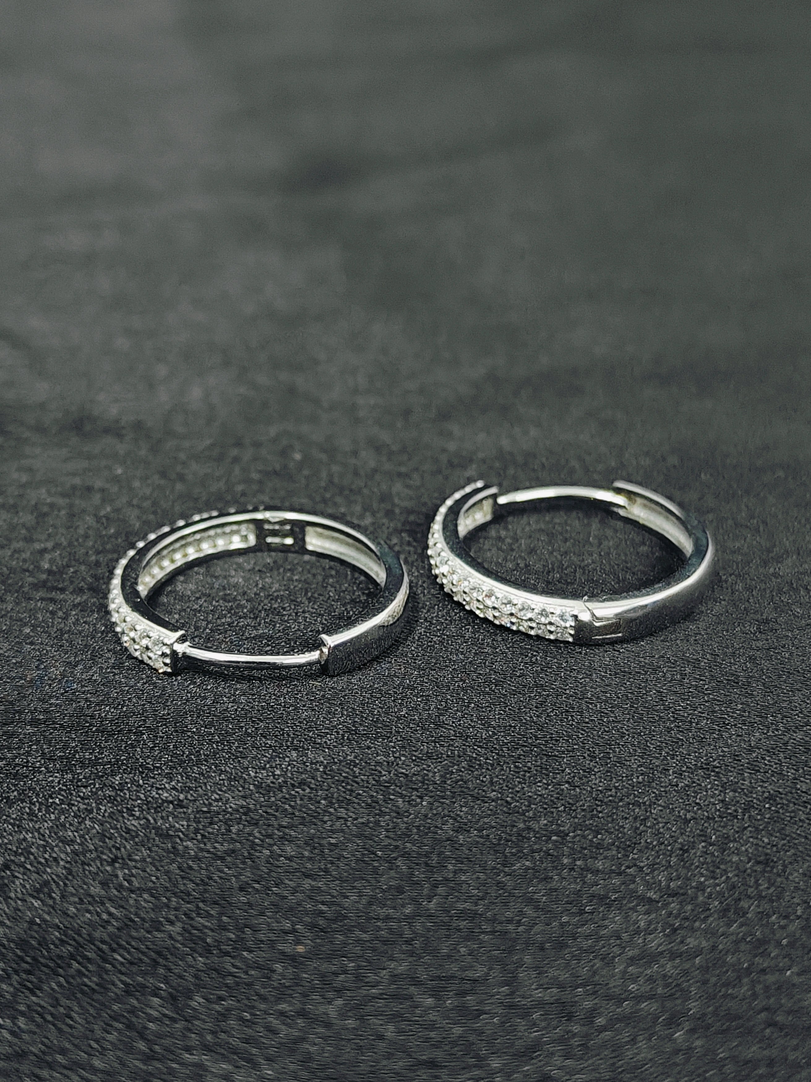Two silver hoop earrings on a dark textured surface