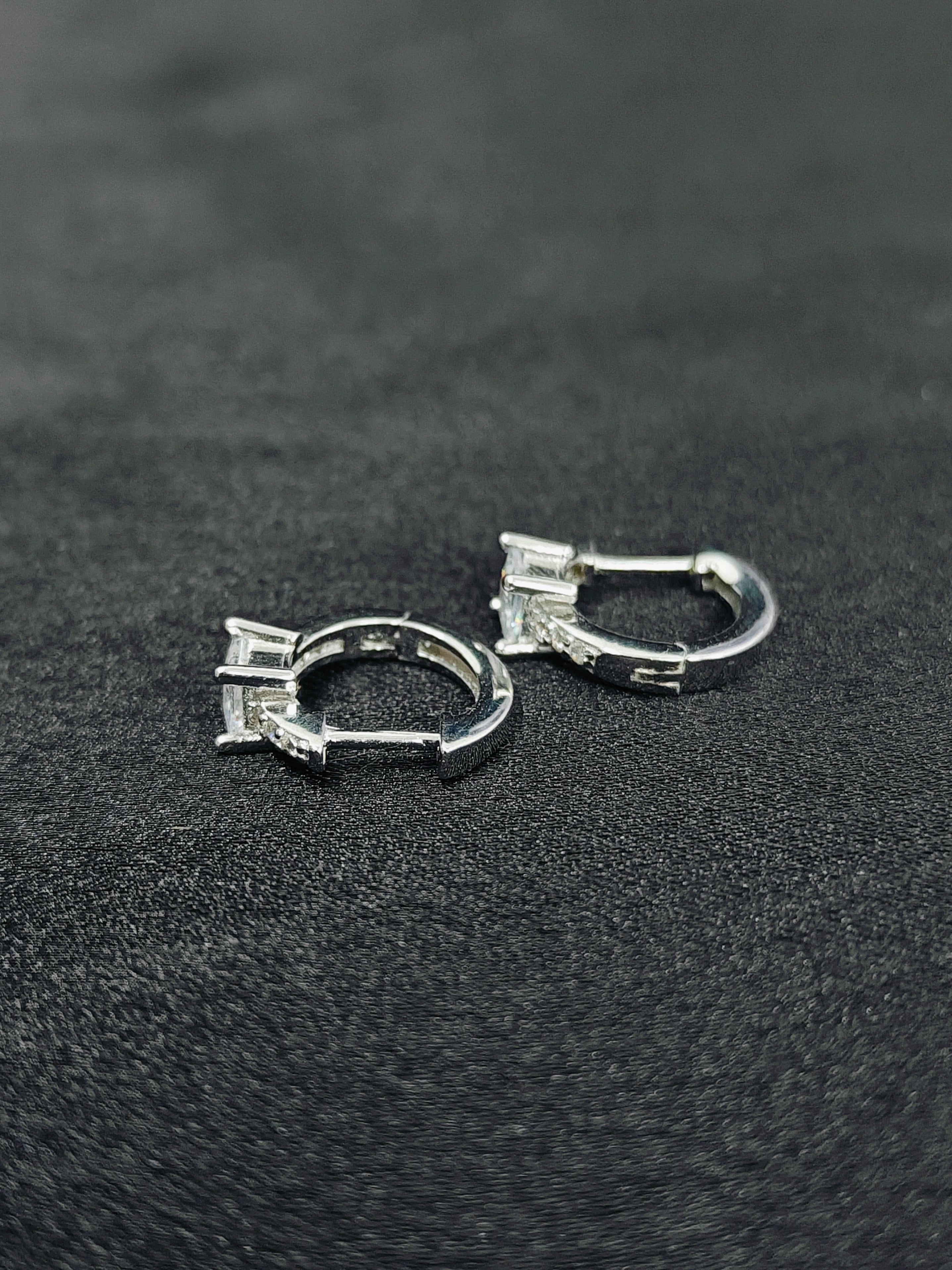 Pair of silver hoop earrings on a black textured surface