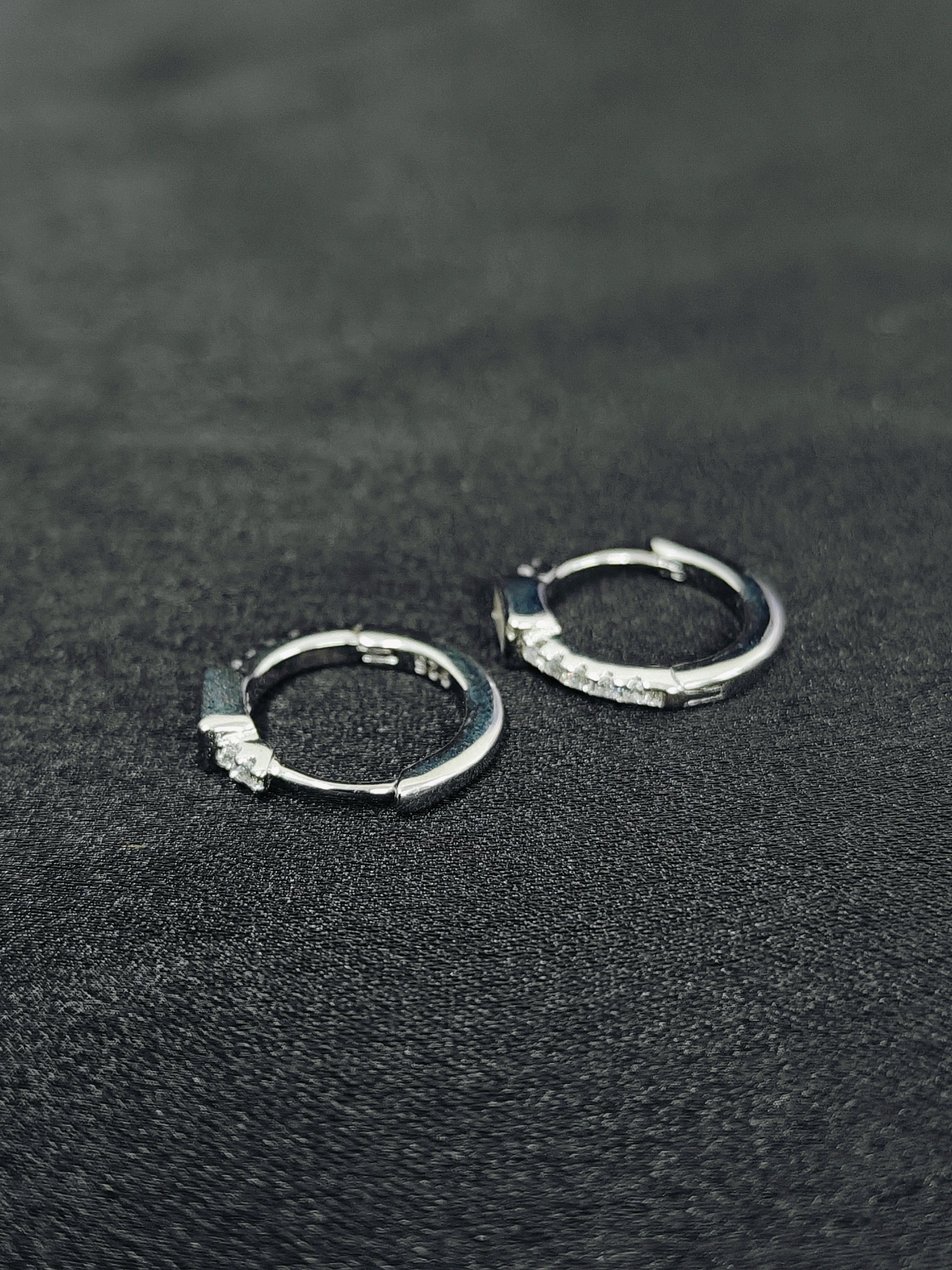 Pair of silver hoop earrings on a black textured surface