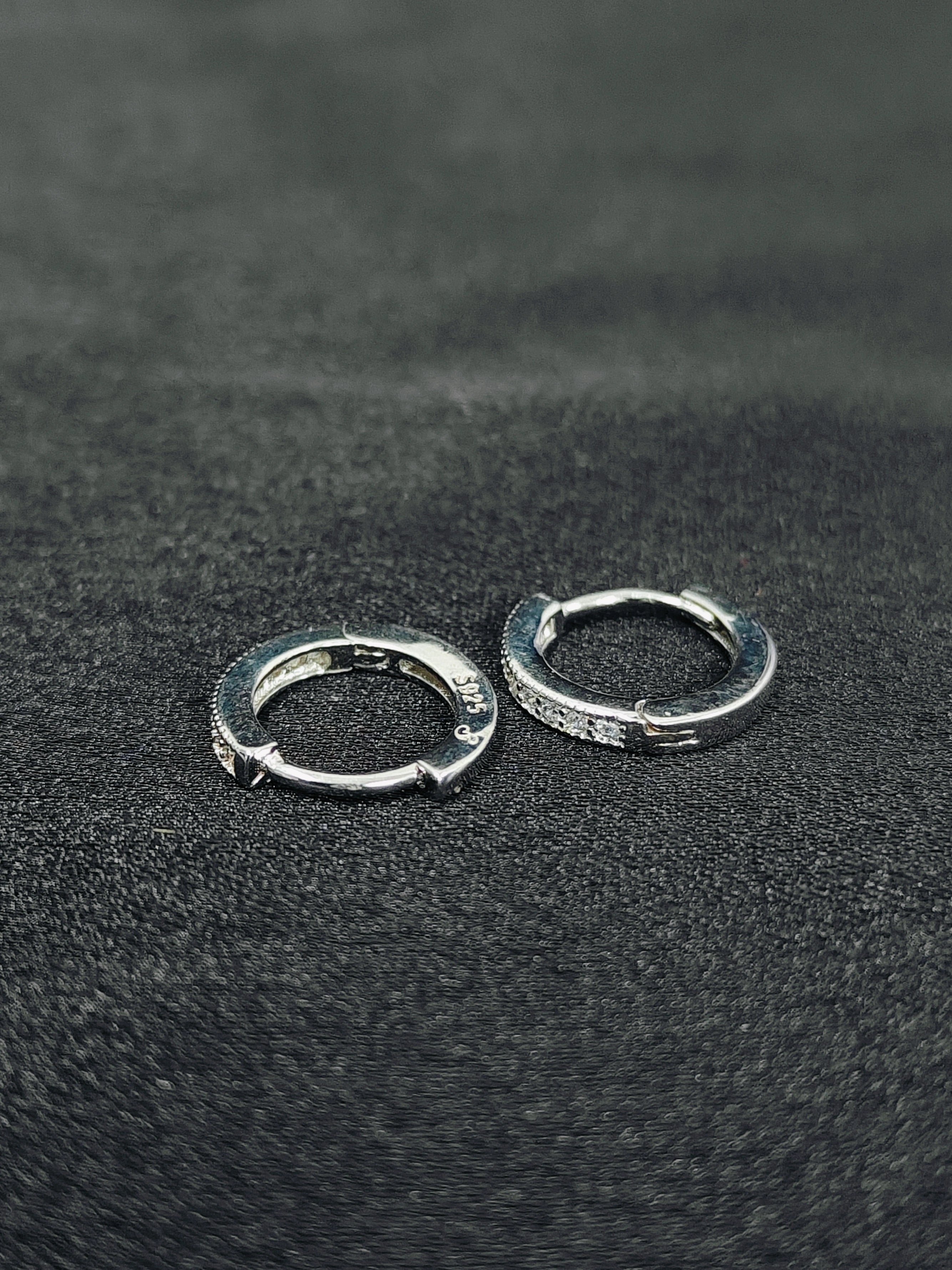 Two silver hoop earrings on a textured black surface
