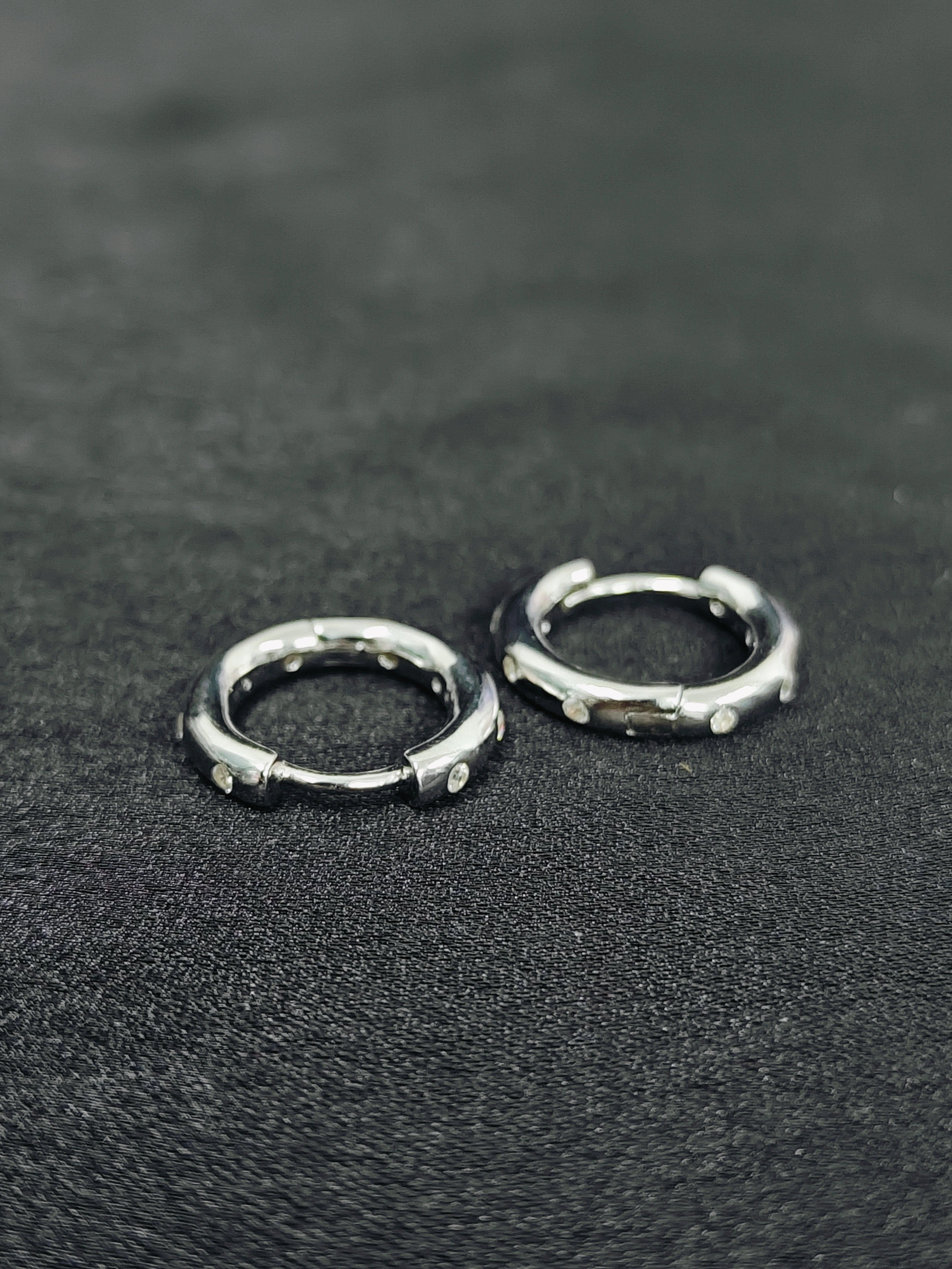 Two silver hoop earrings on a dark textured surface