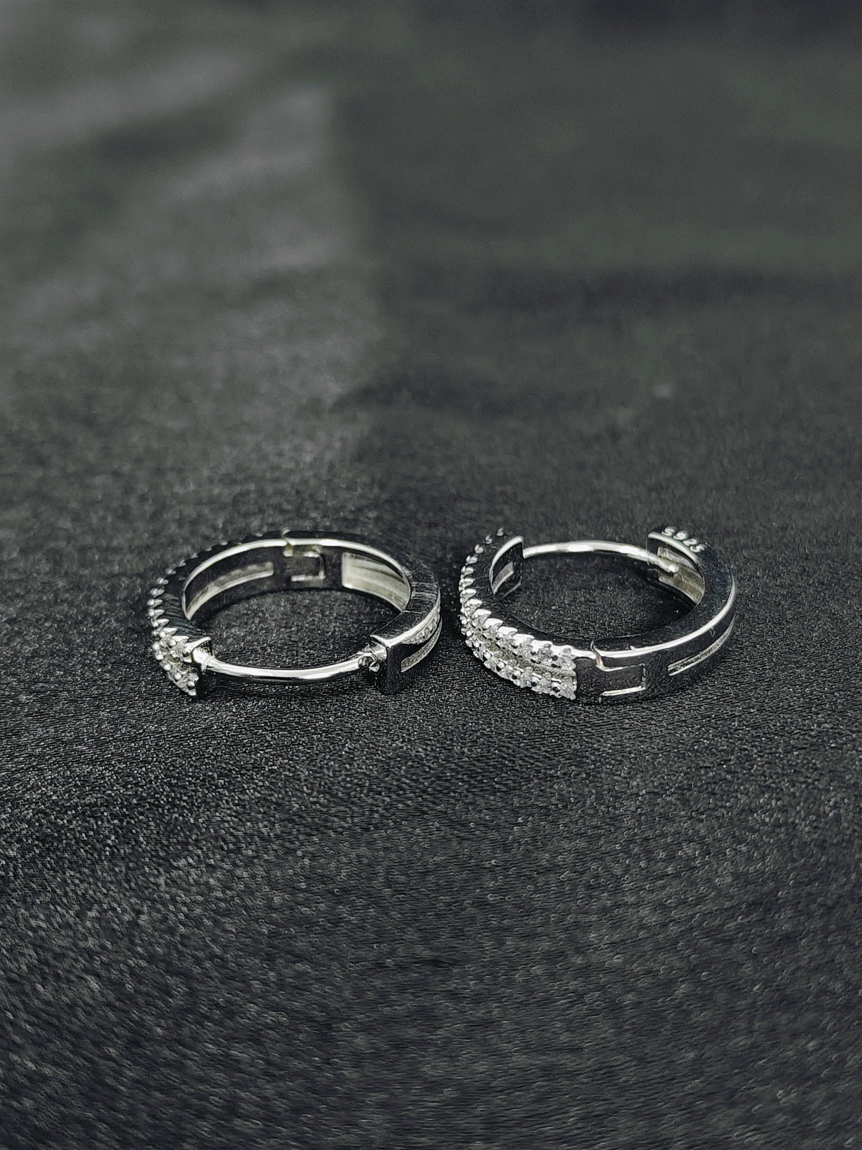 Two silver hoop earrings on a black textured surface