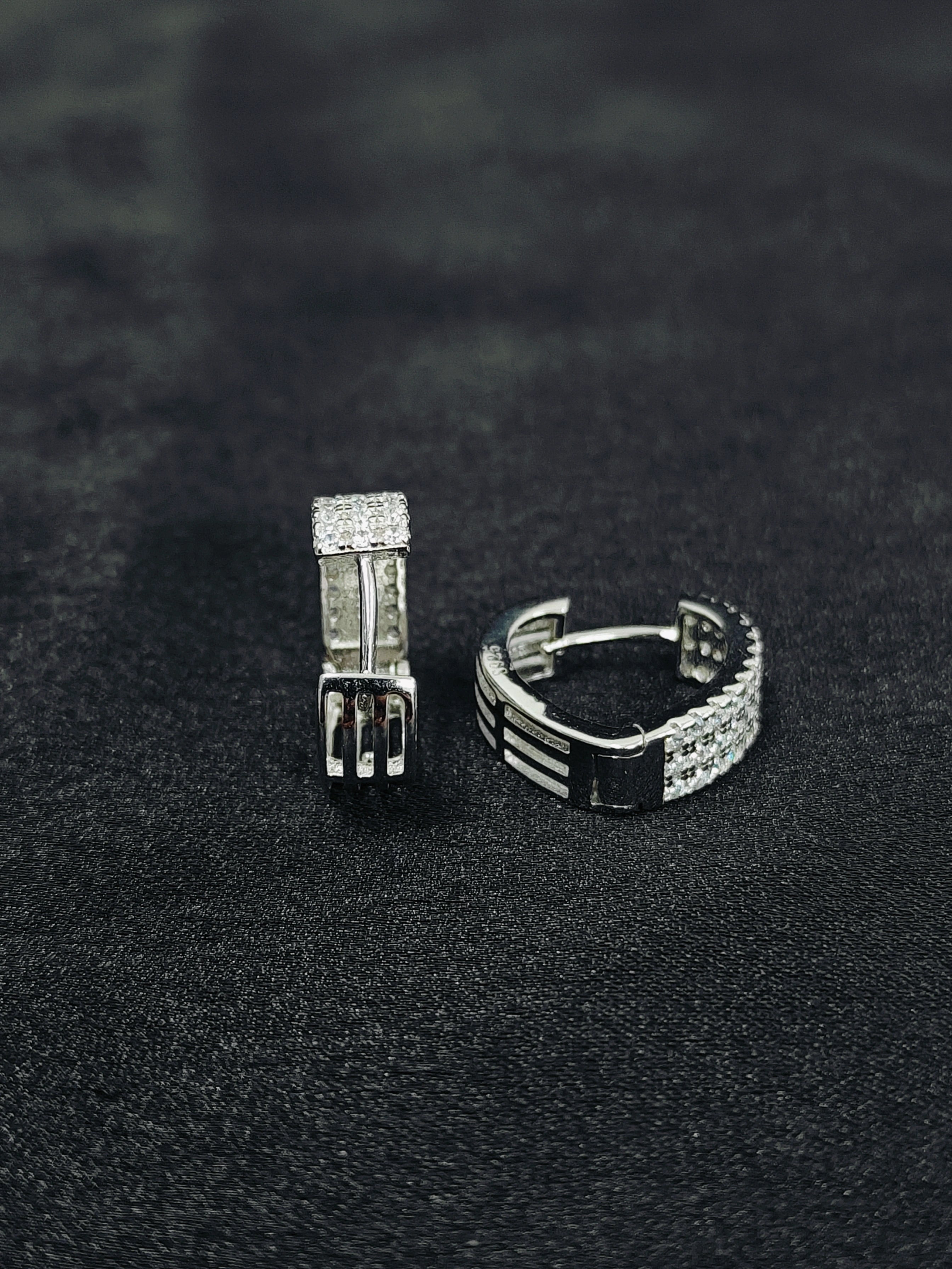 Two silver hoop earrings on a black textured surface