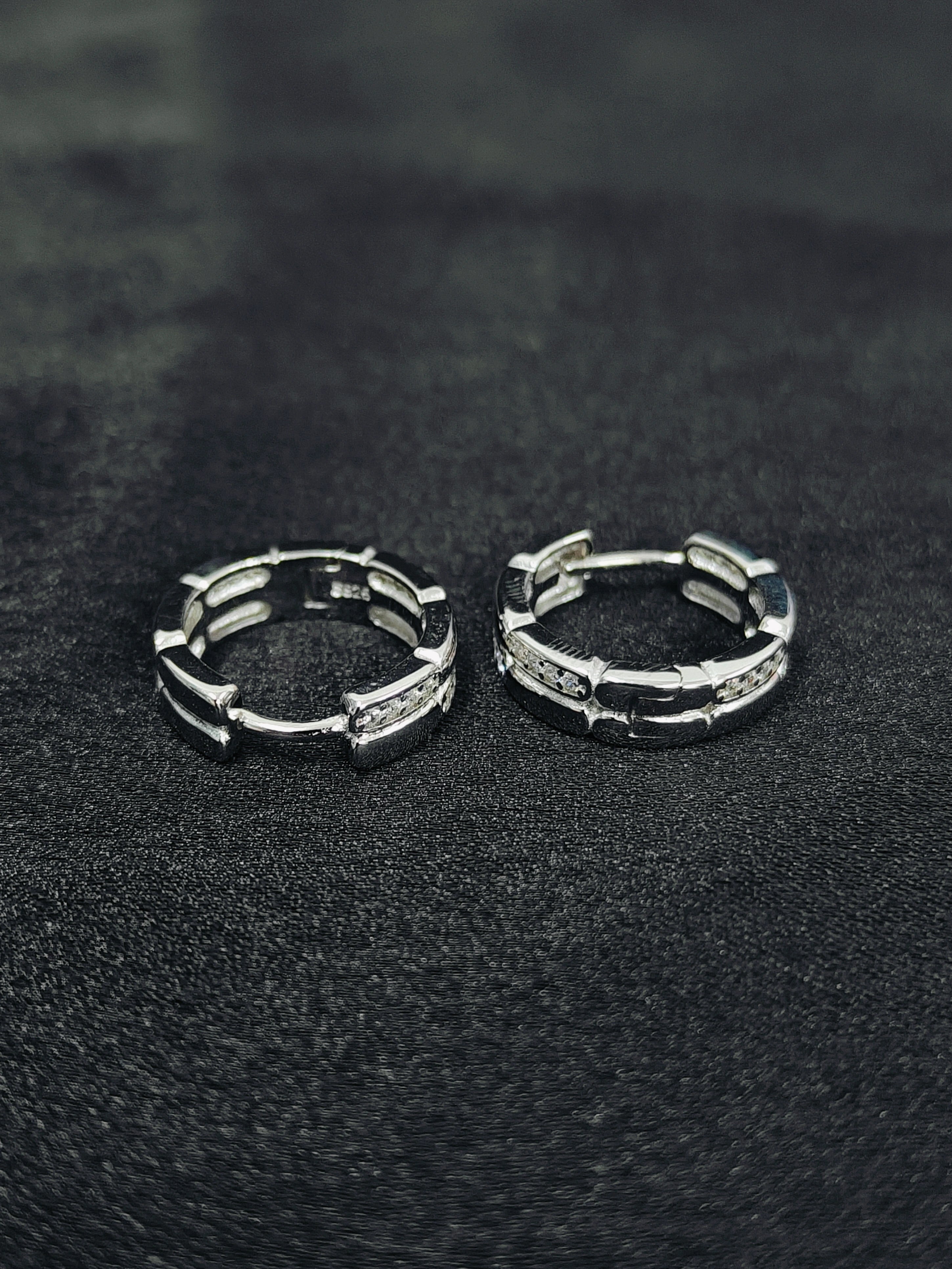 Pair of silver hoop earrings on a black textured surface