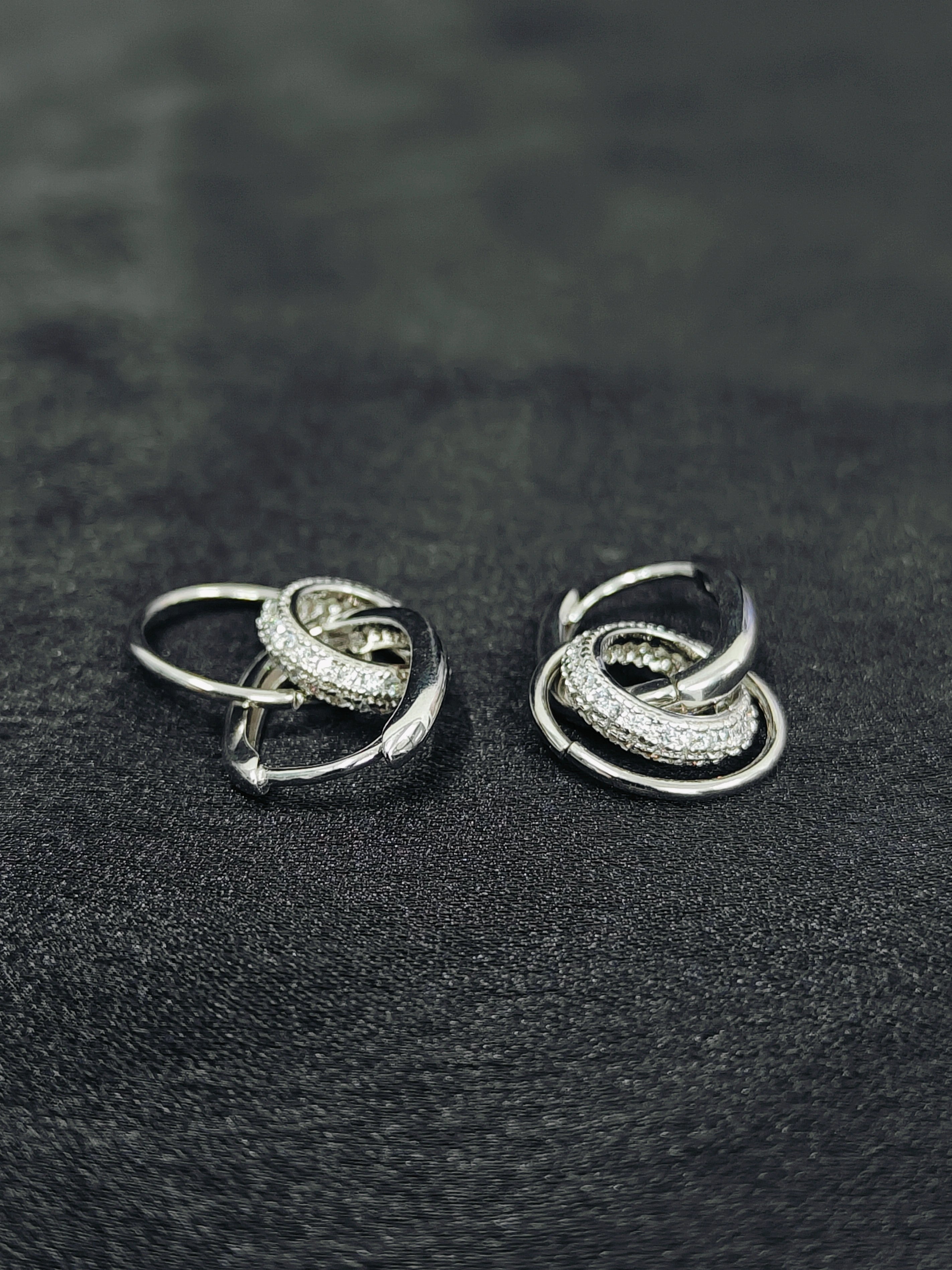 Pair of silver hoop earrings with embedded stones on a black textured surface