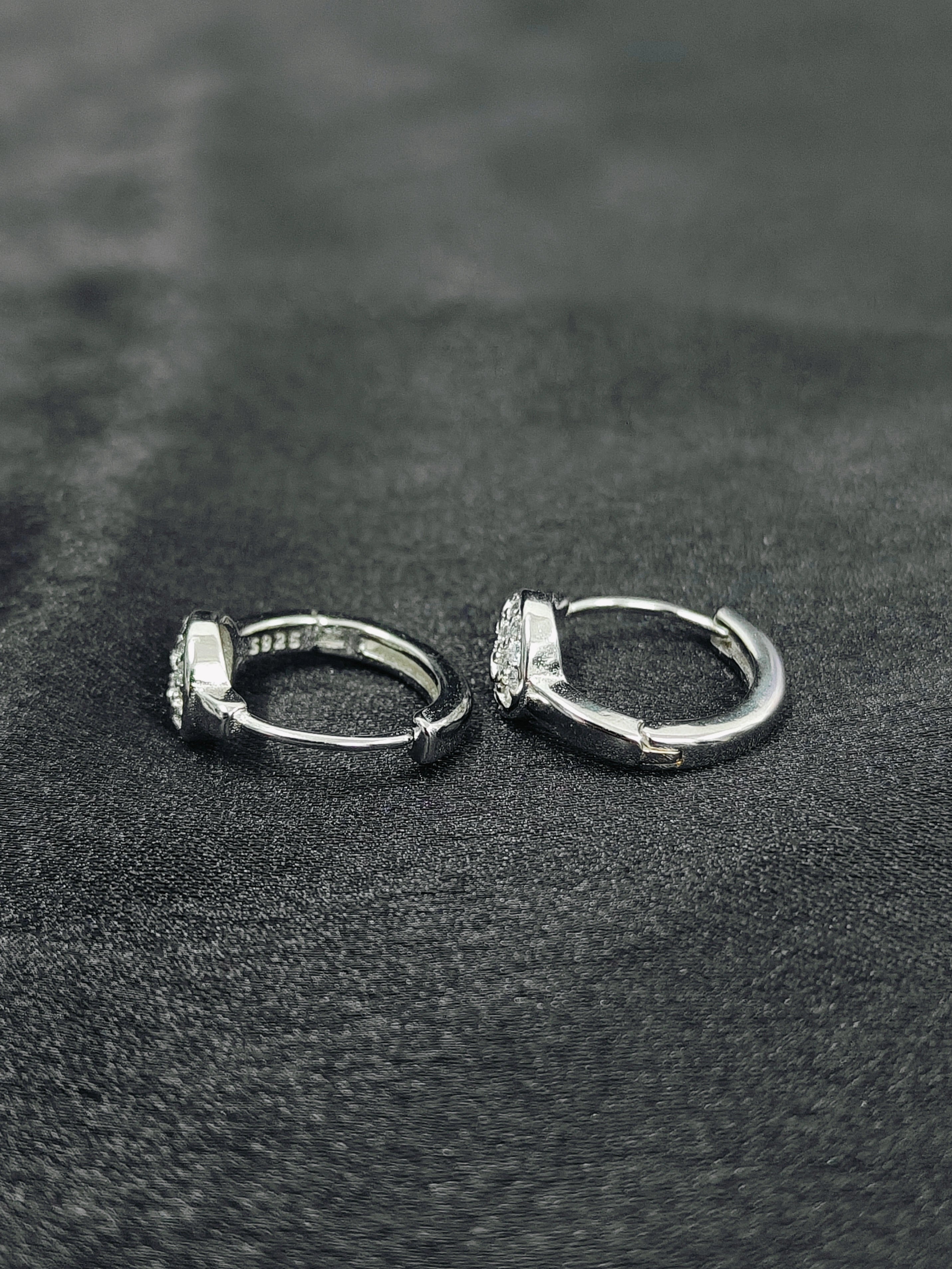 Two silver hoop earrings on a textured black surface