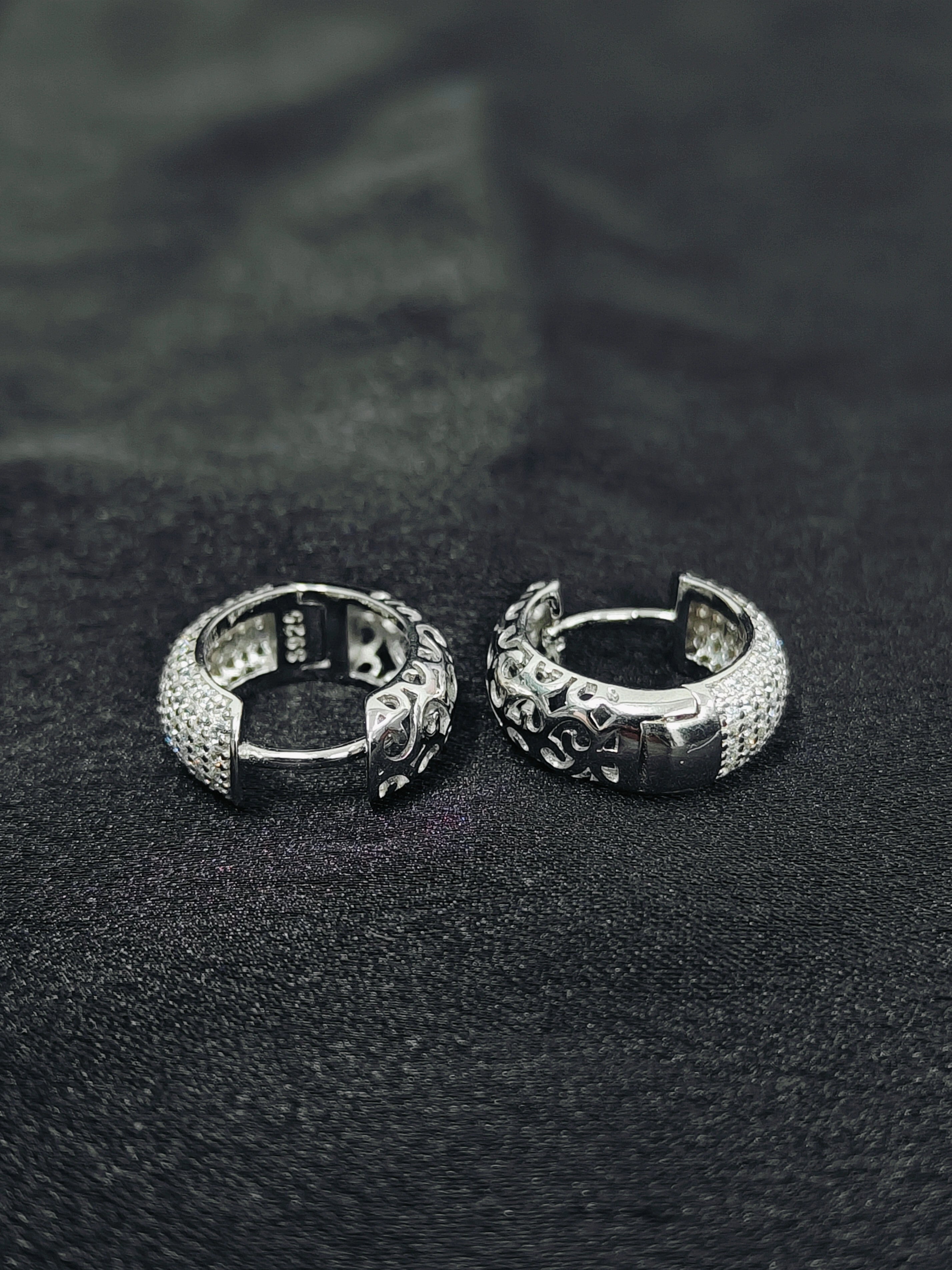 Two silver hoop earrings on a black textured surface