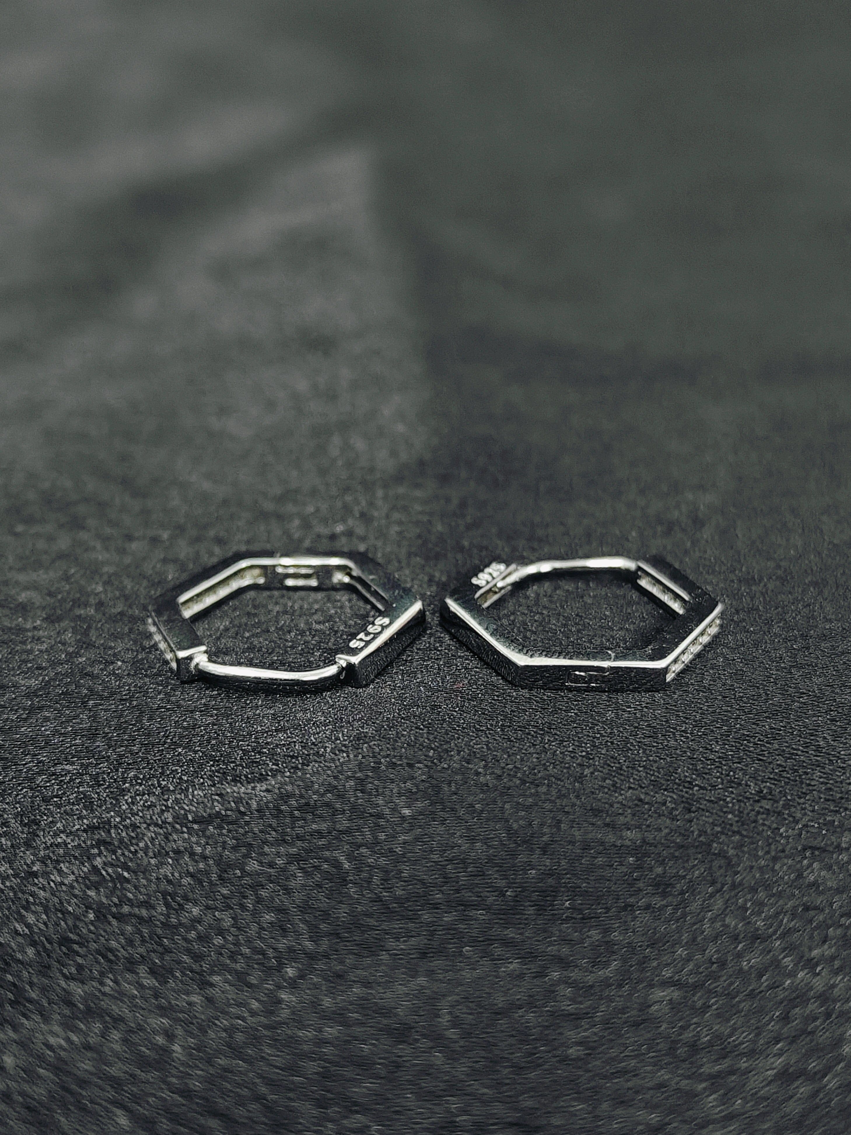 Hexagonal hoop earrings on a textured black surface