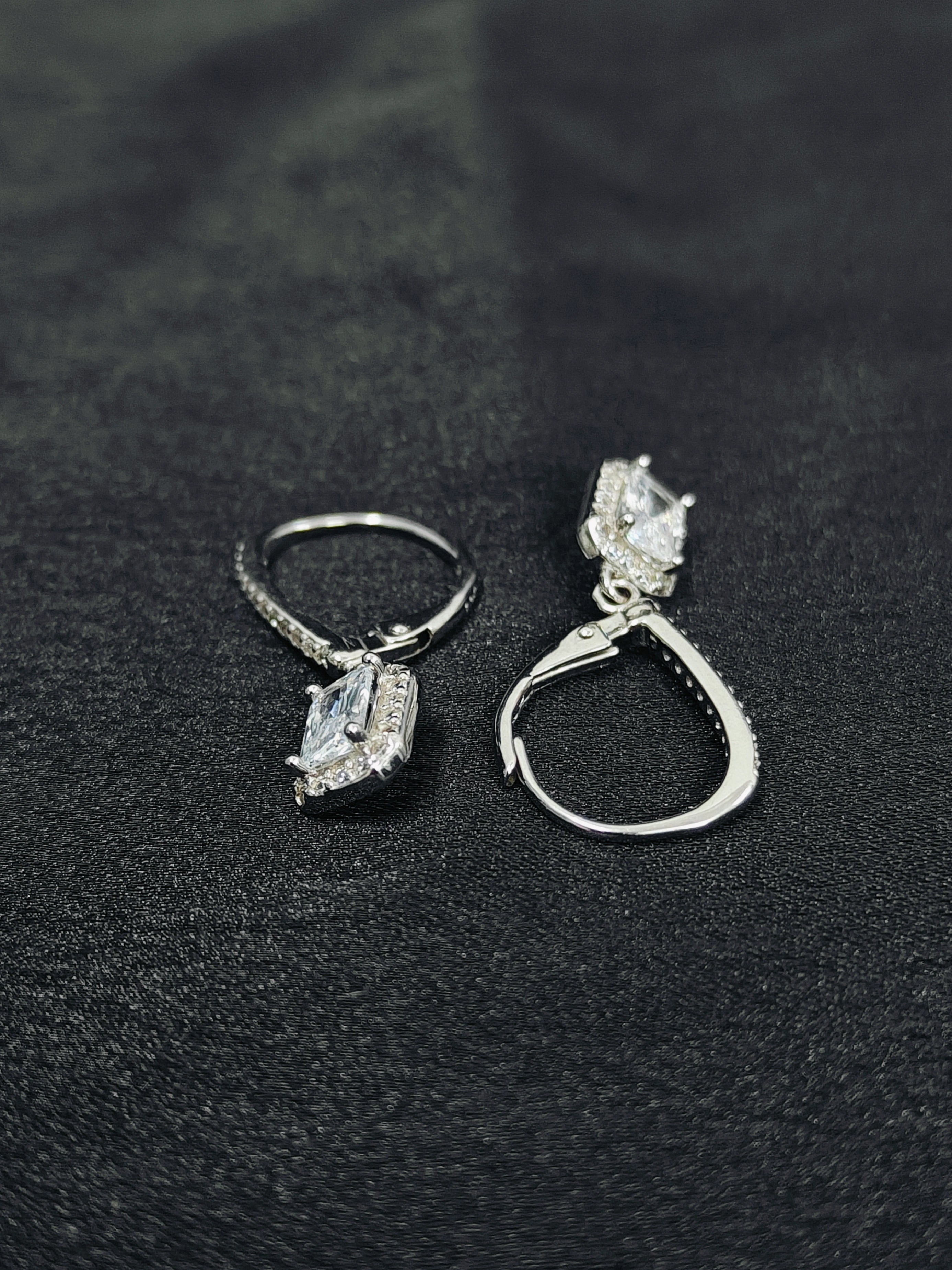 Pair of silver earrings with gemstones on a black textured surface