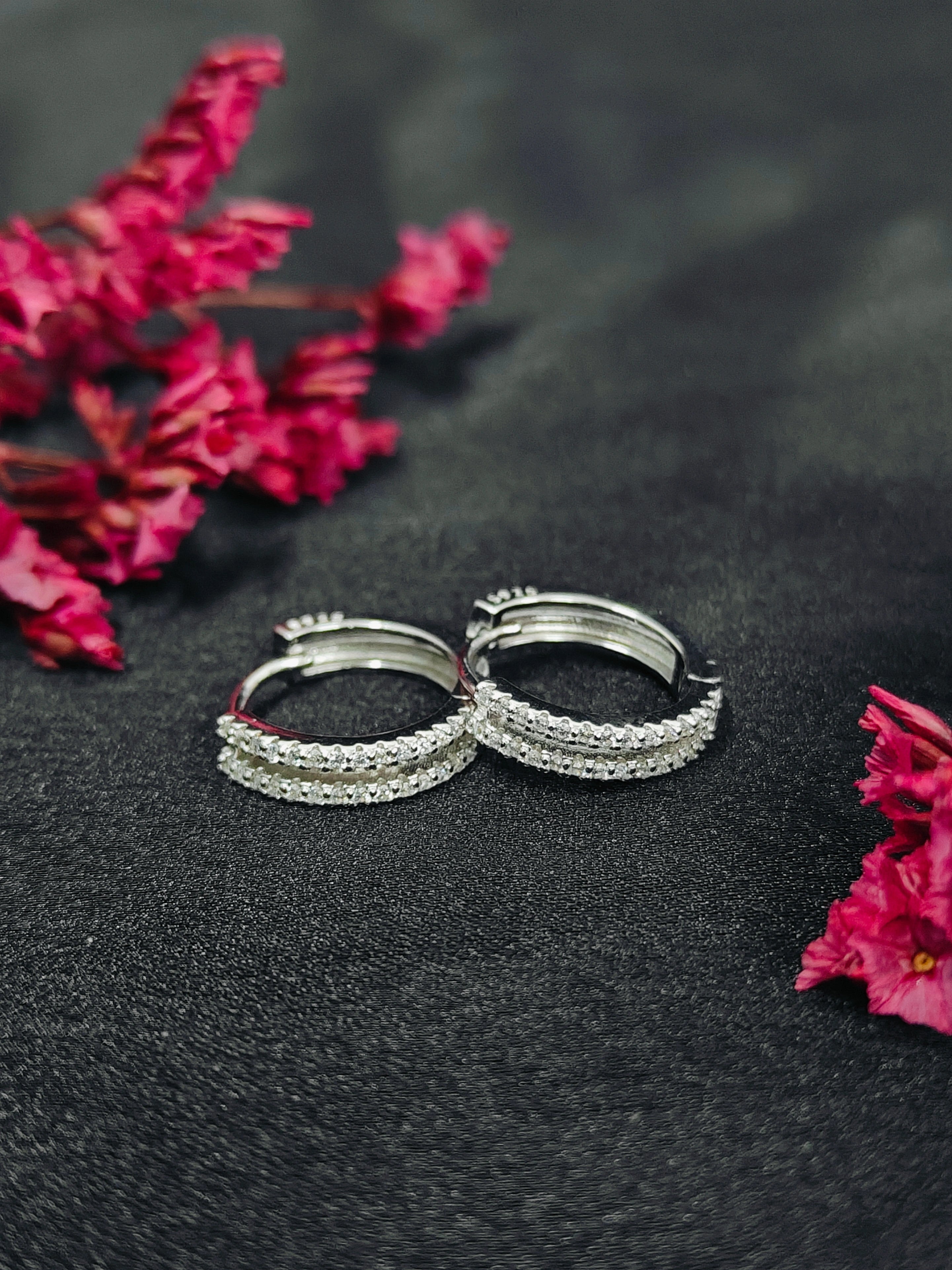 Silver hoop earrings on a dark surface with pink flowers