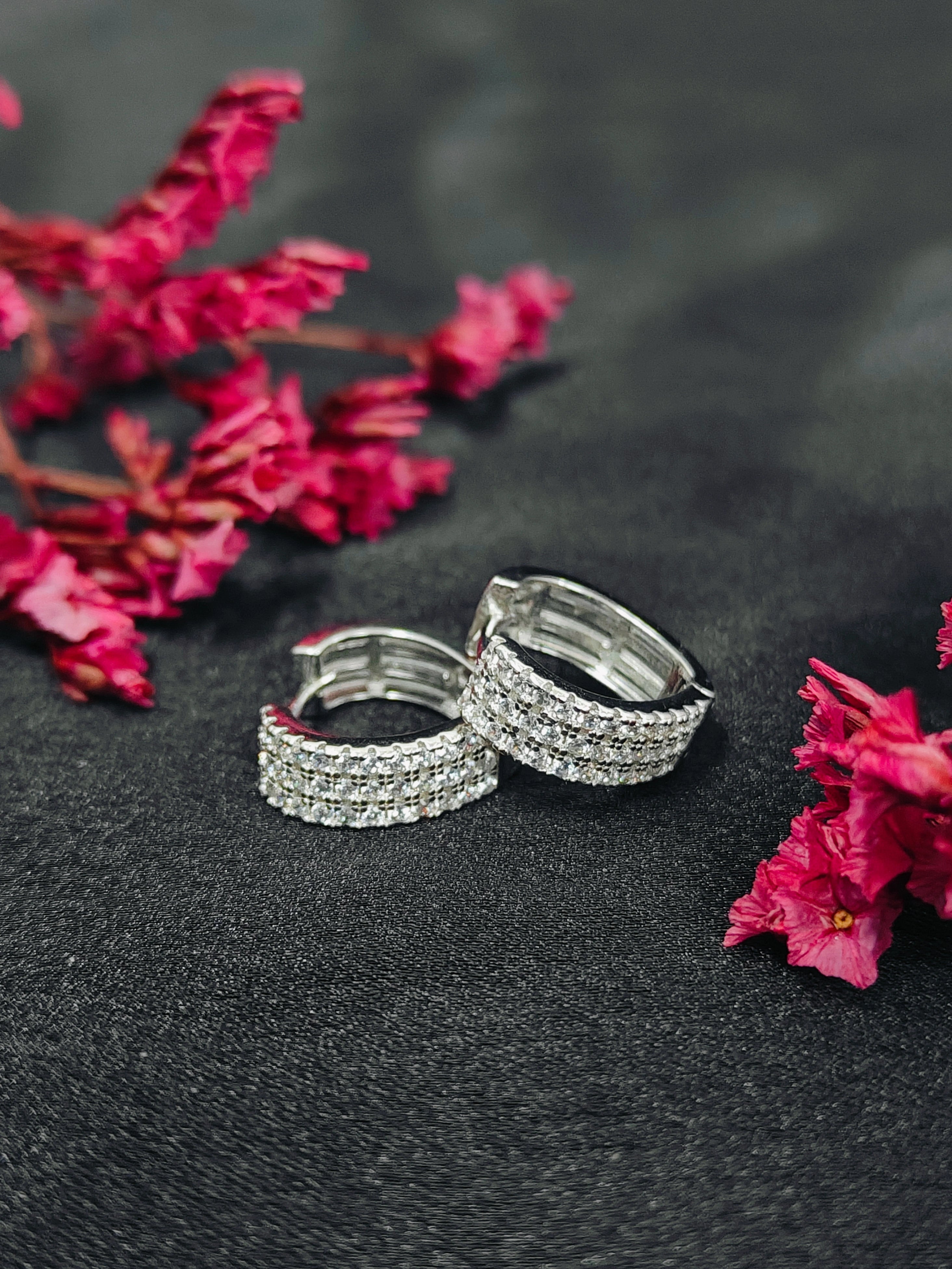 Silver hoop earrings on a dark surface with pink flowers