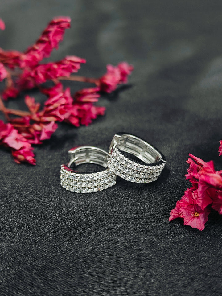 Silver hoop earrings on a dark surface with pink flowers