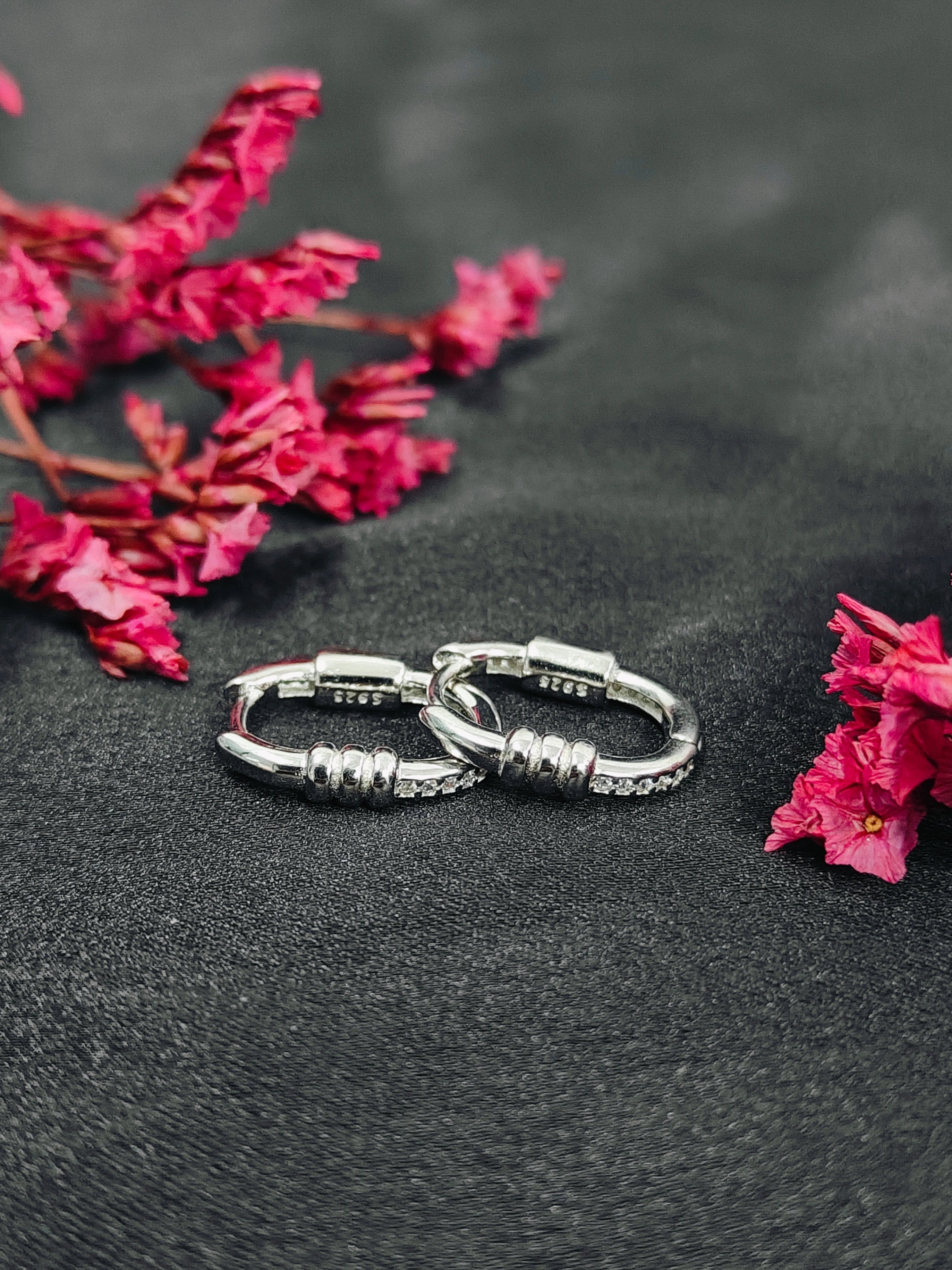 Silver hoop earrings on a dark surface with pink flowers.