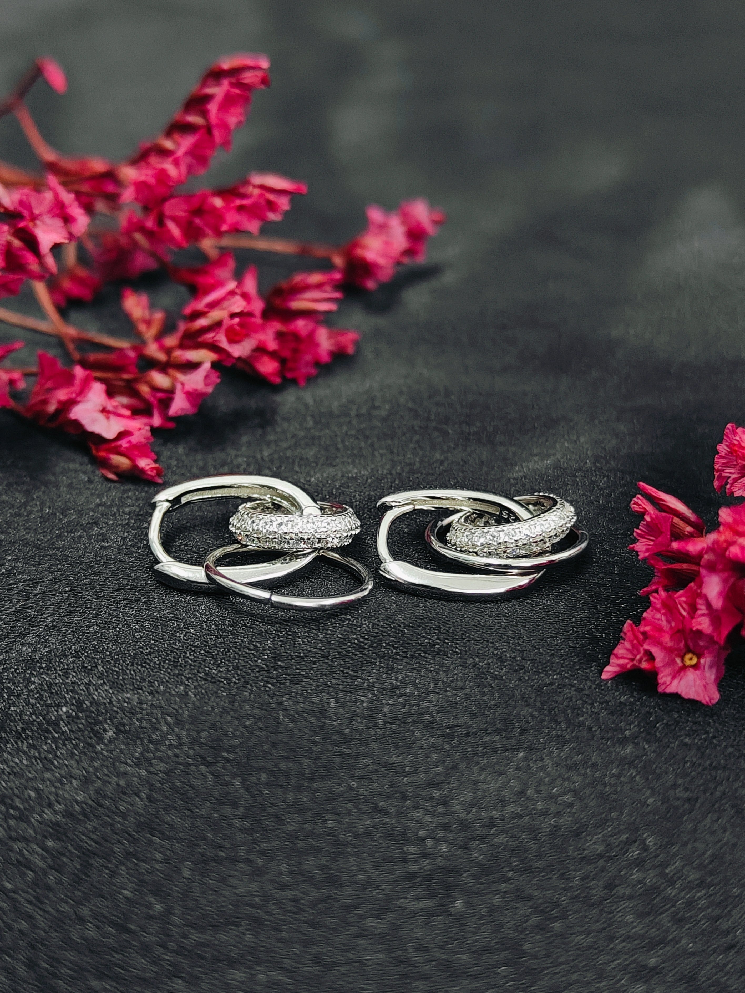 Pair of silver hoop earrings on a dark surface with pink flowers.