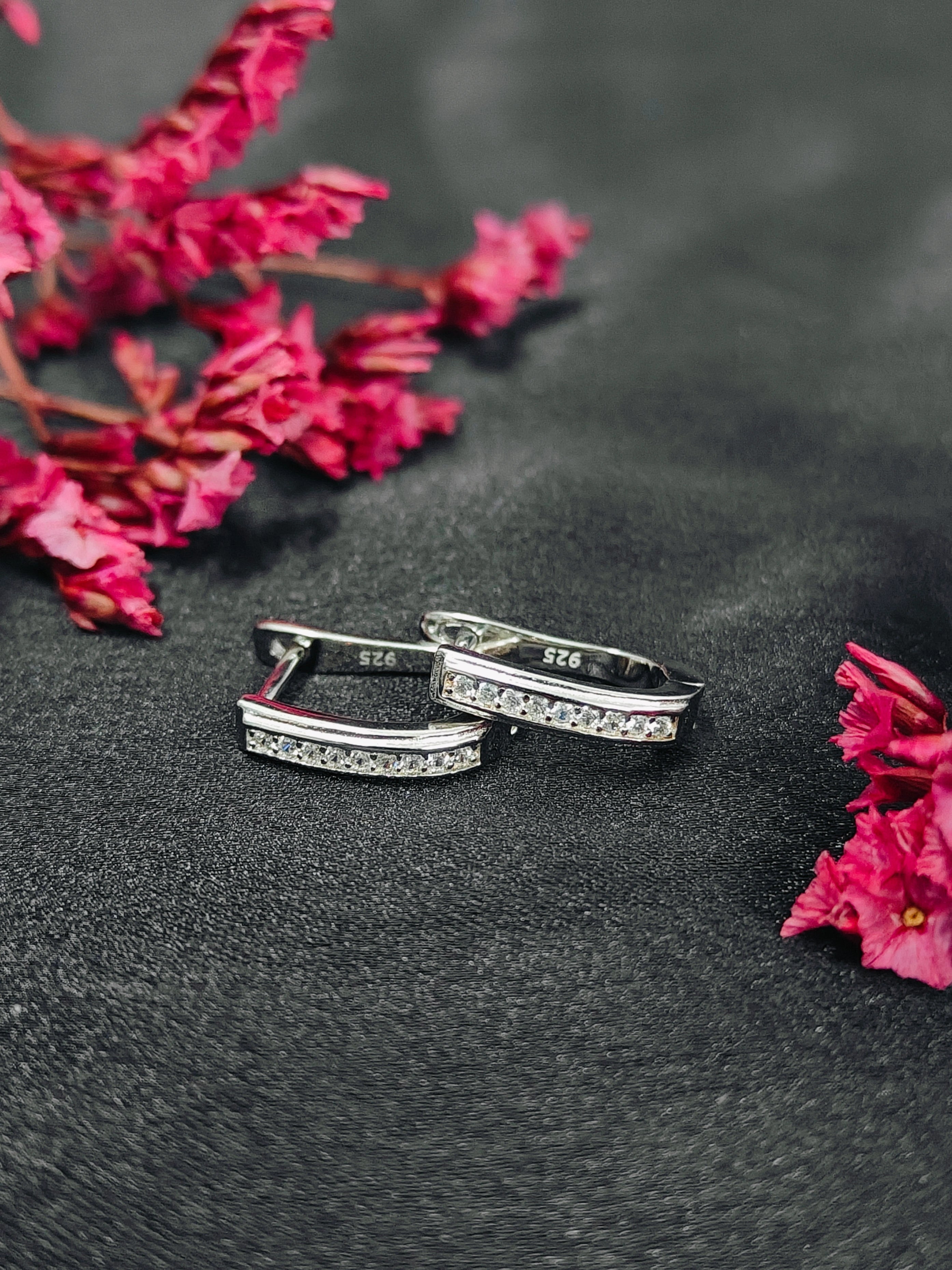 Silver rings with embedded stones on a dark surface with pink flowers.