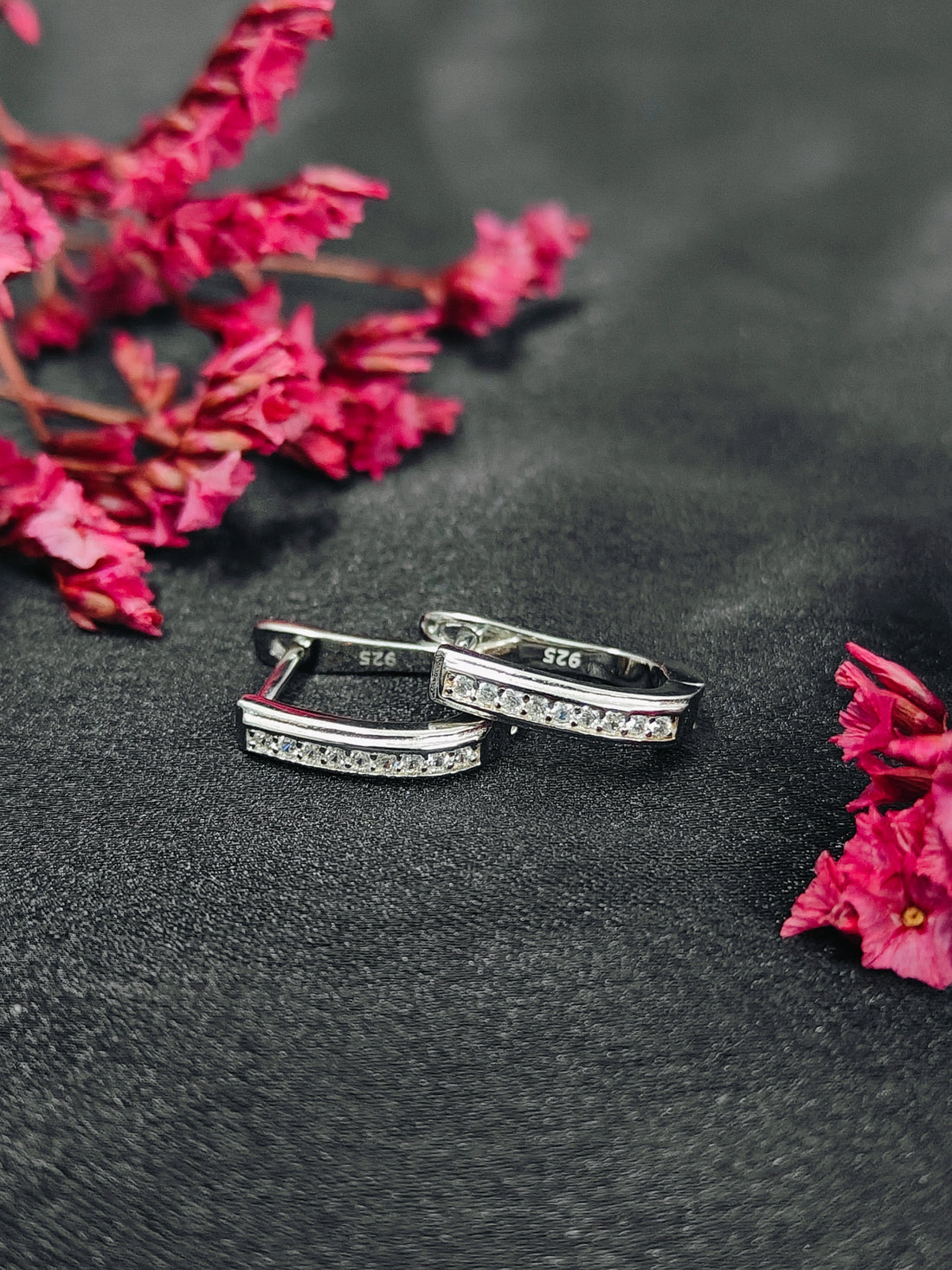 Silver rings with embedded stones on a dark surface with pink flowers.