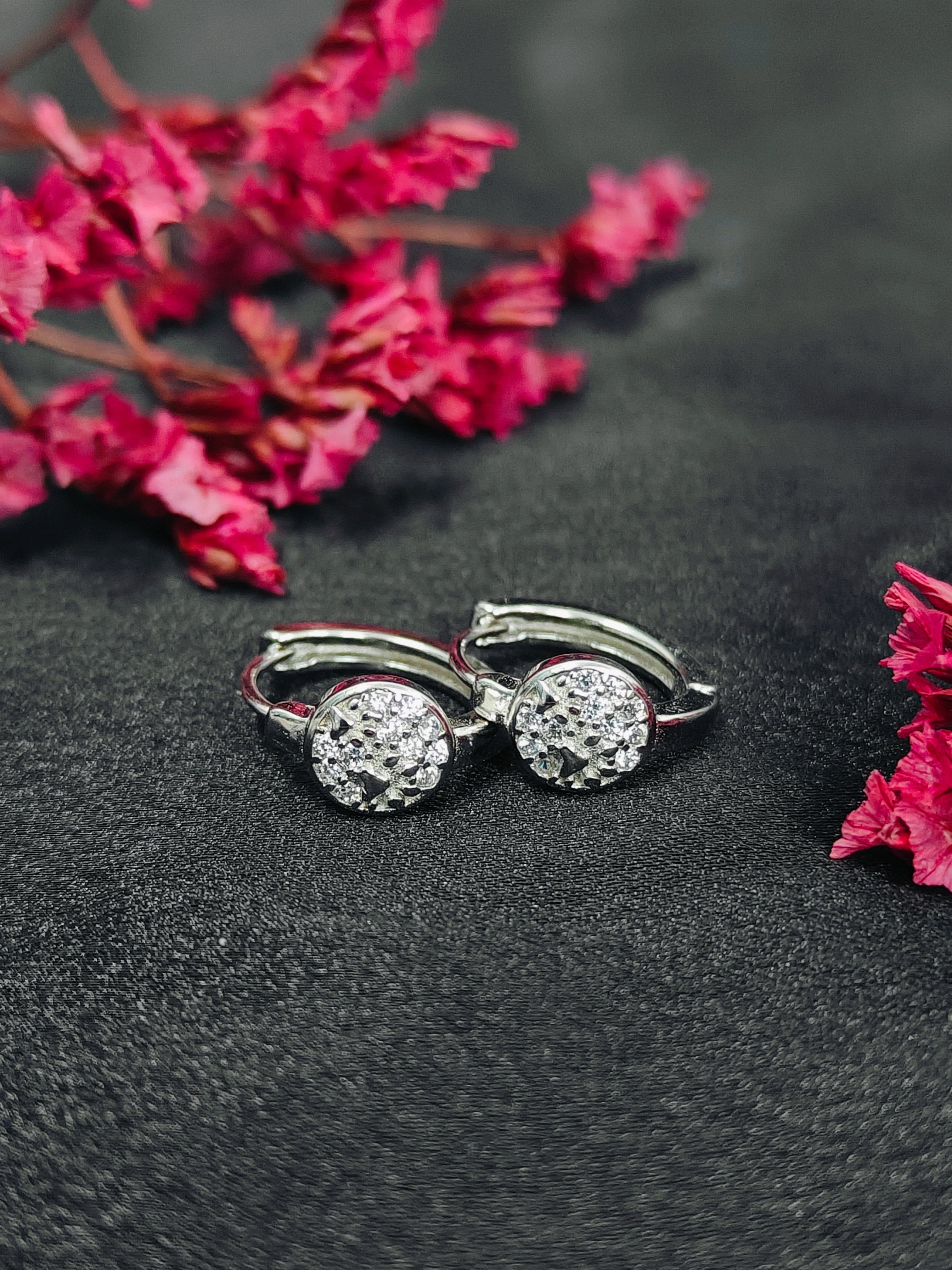 Silver earrings with clear stones on a dark surface with pink flowers.