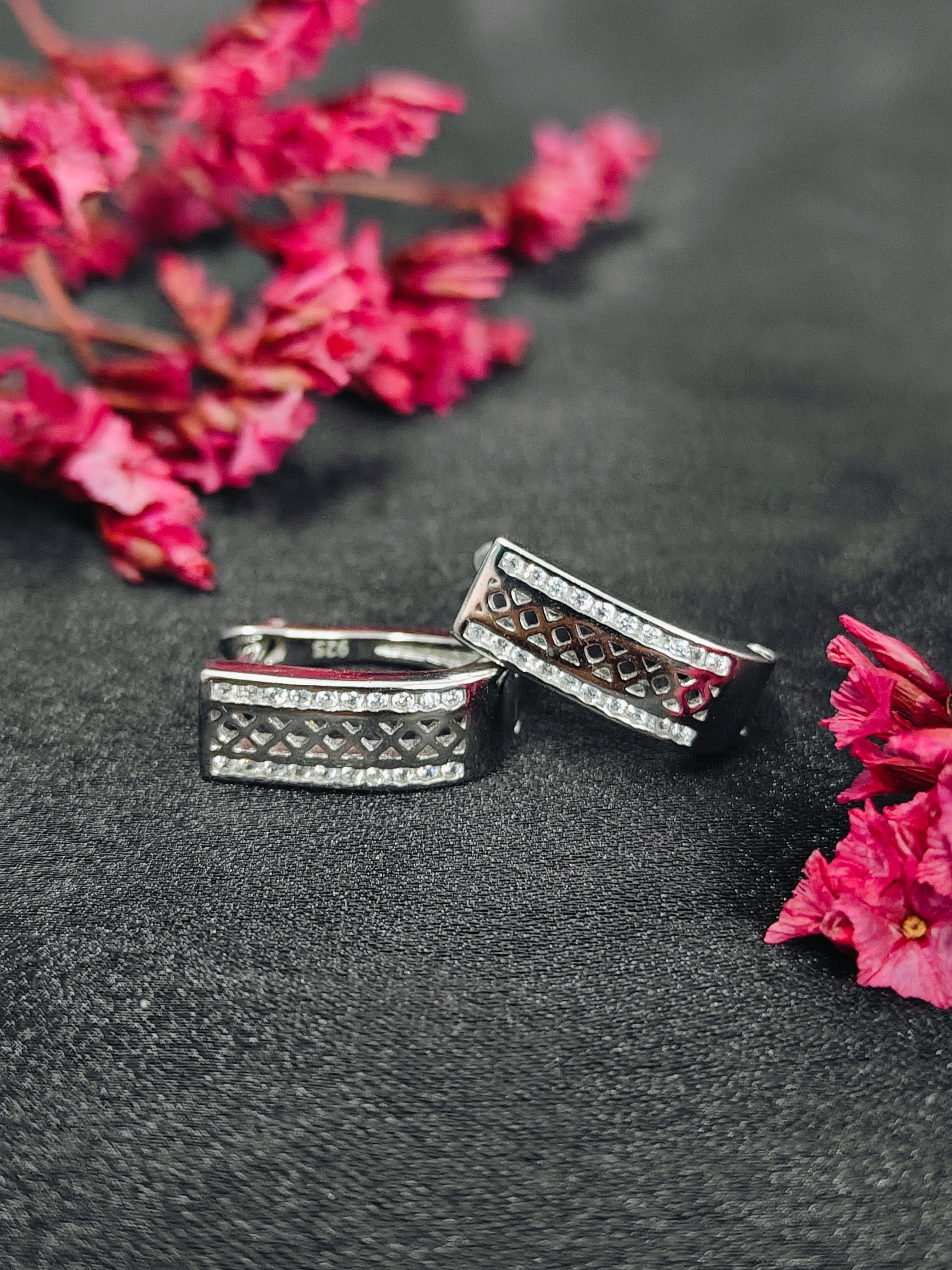 Two silver rings with gemstones on a dark surface with pink flowers.