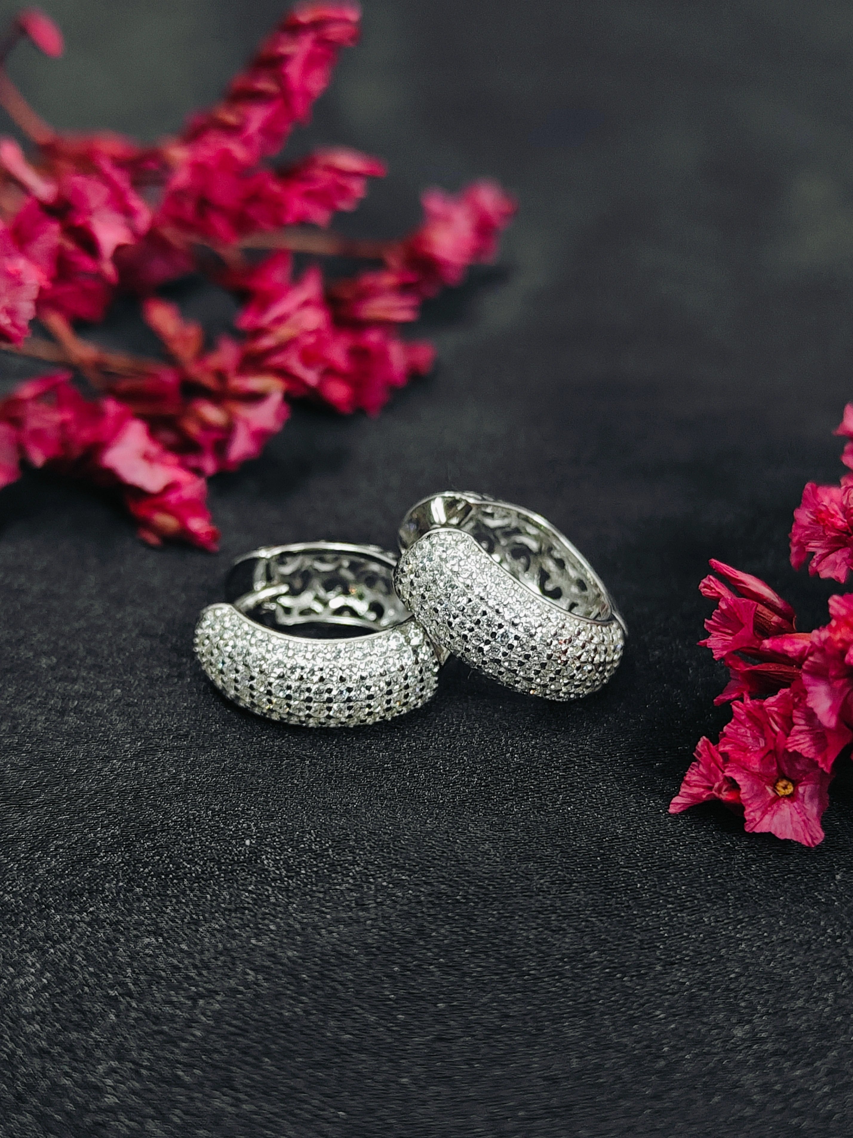 Silver rings with pink flowers on a dark surface