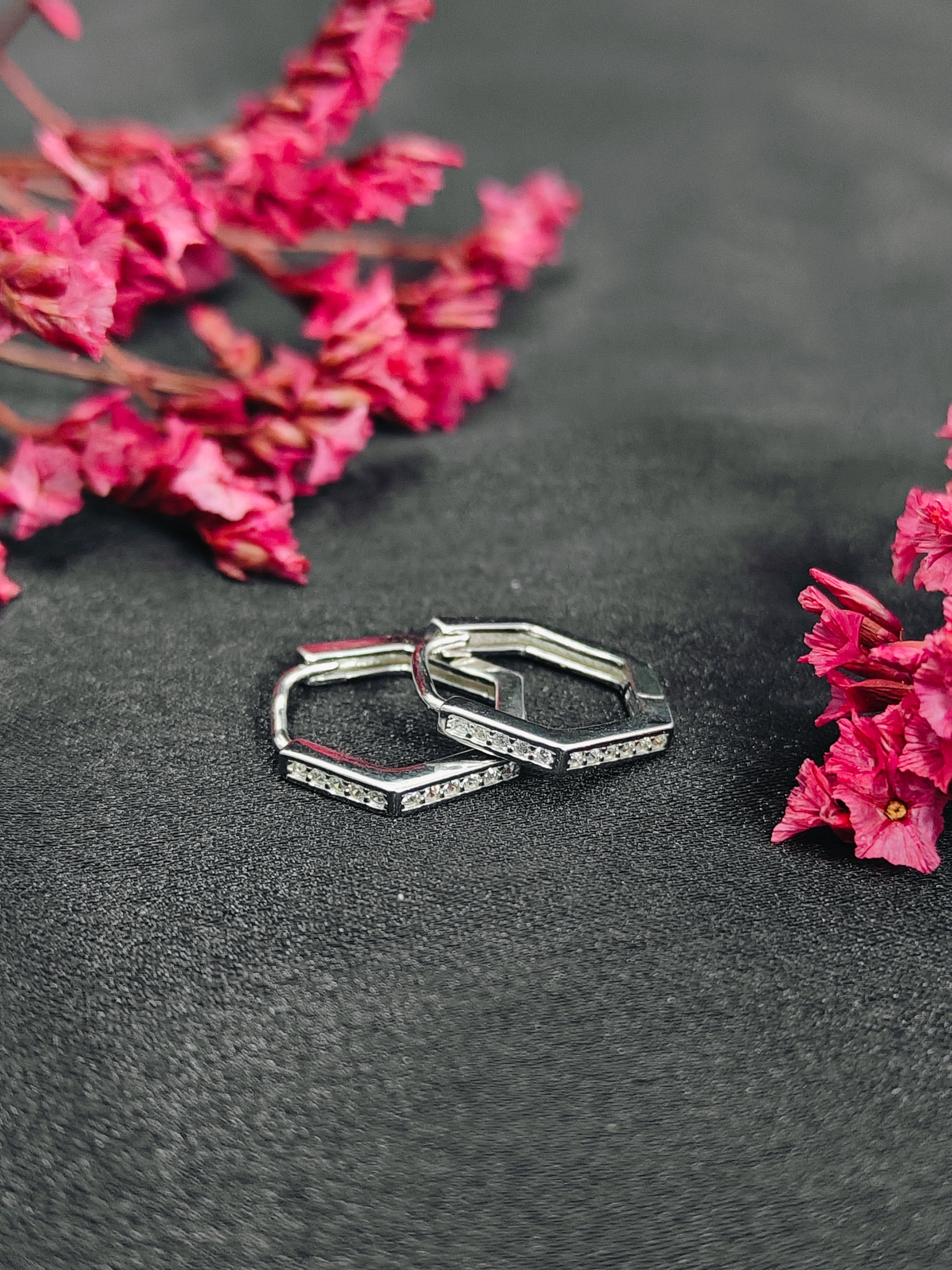 Silver hoop earrings with gemstones on a dark surface with pink flowers.