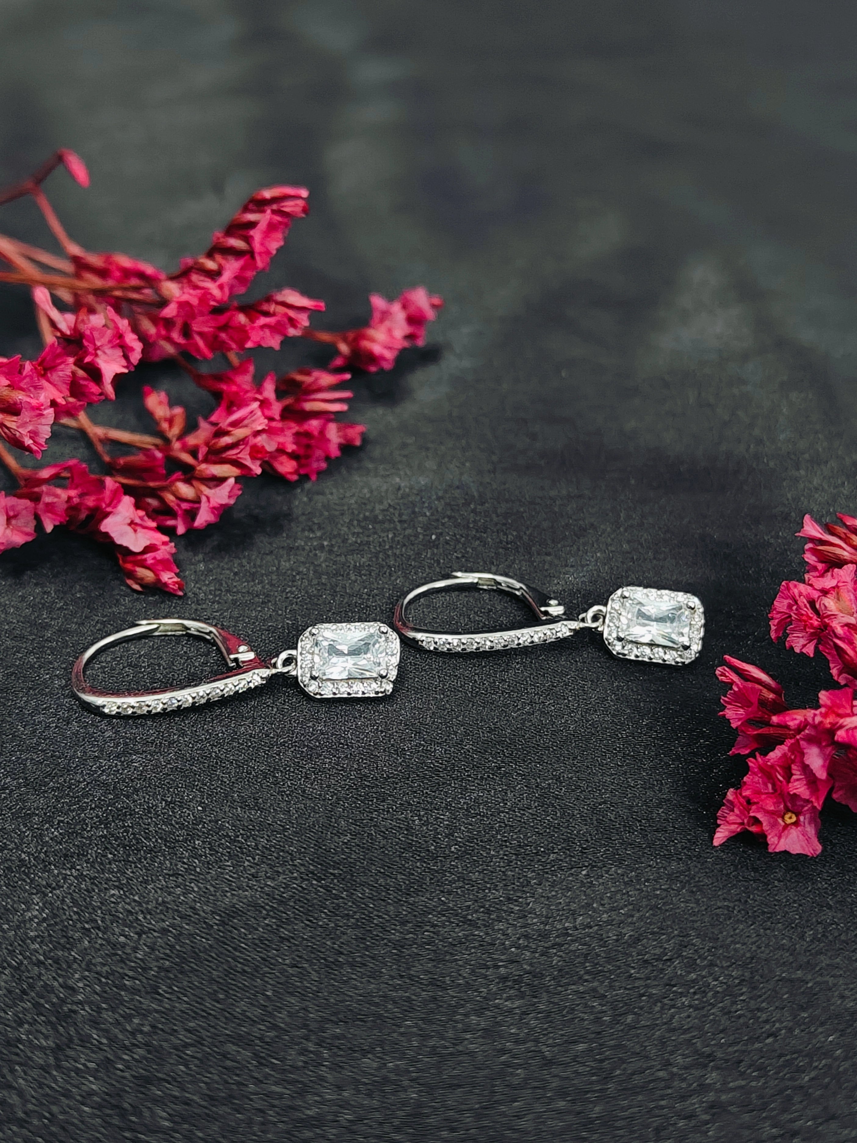 Silver earrings with gemstones on a dark surface with pink flowers