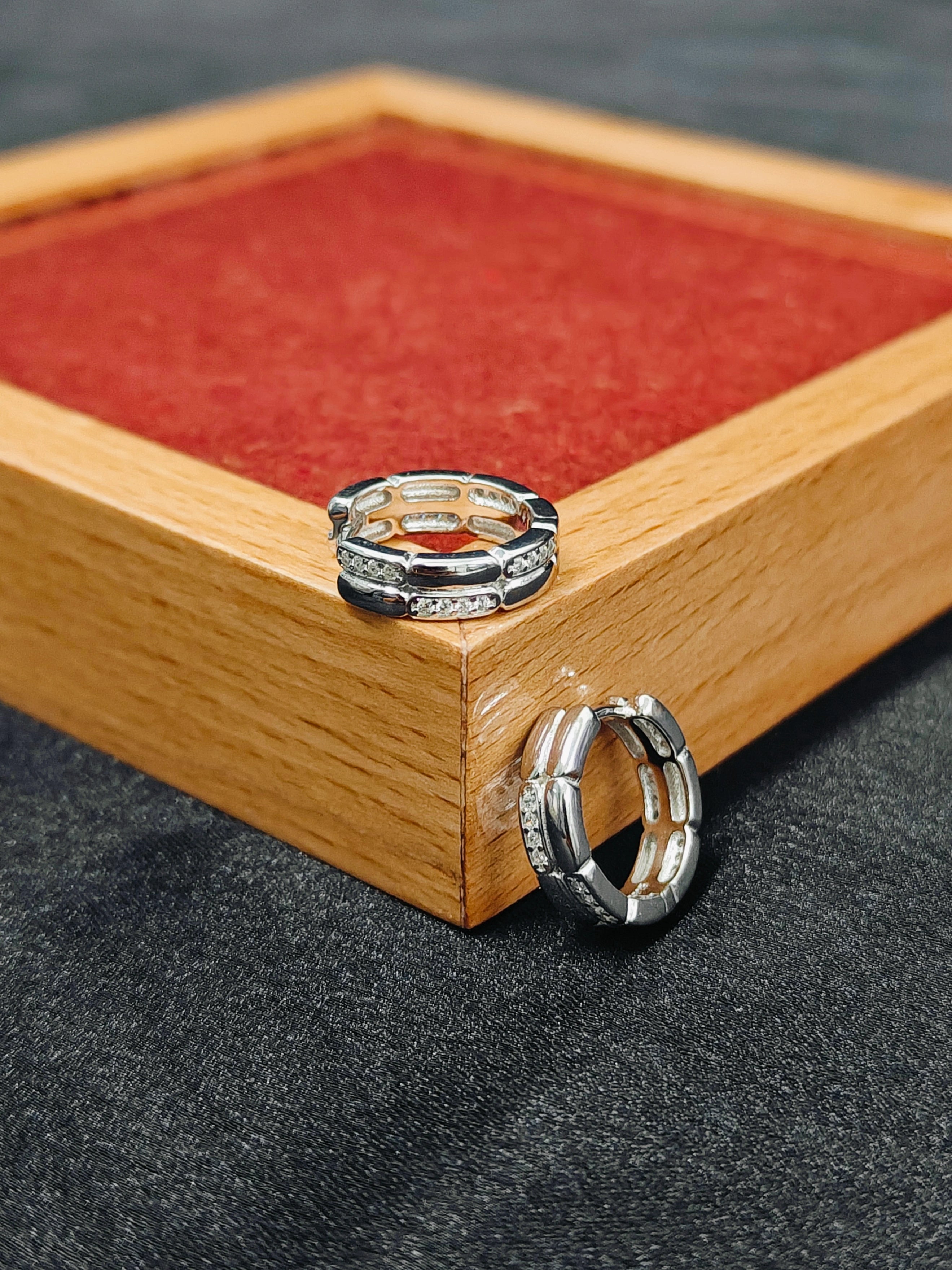 Two silver rings on a wooden box with a red interior.