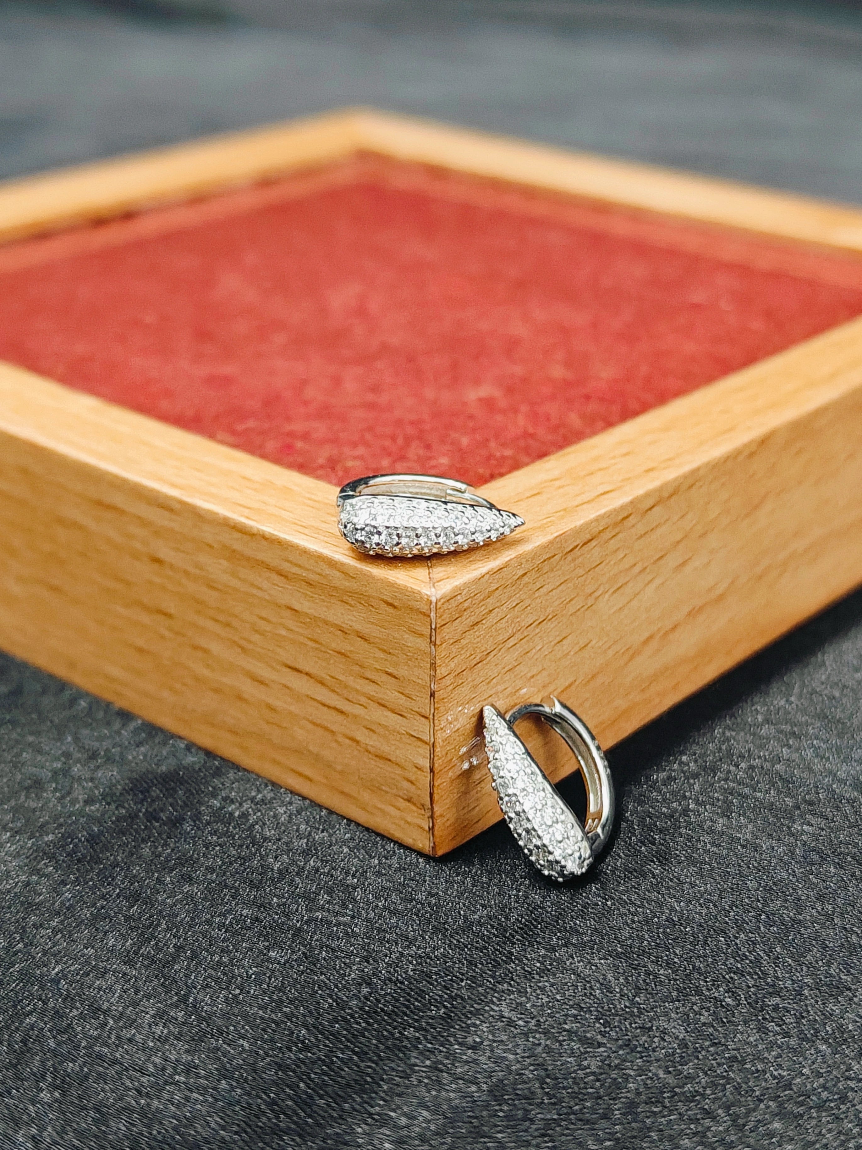 Two silver rings on a wooden jewelry box with red interior.