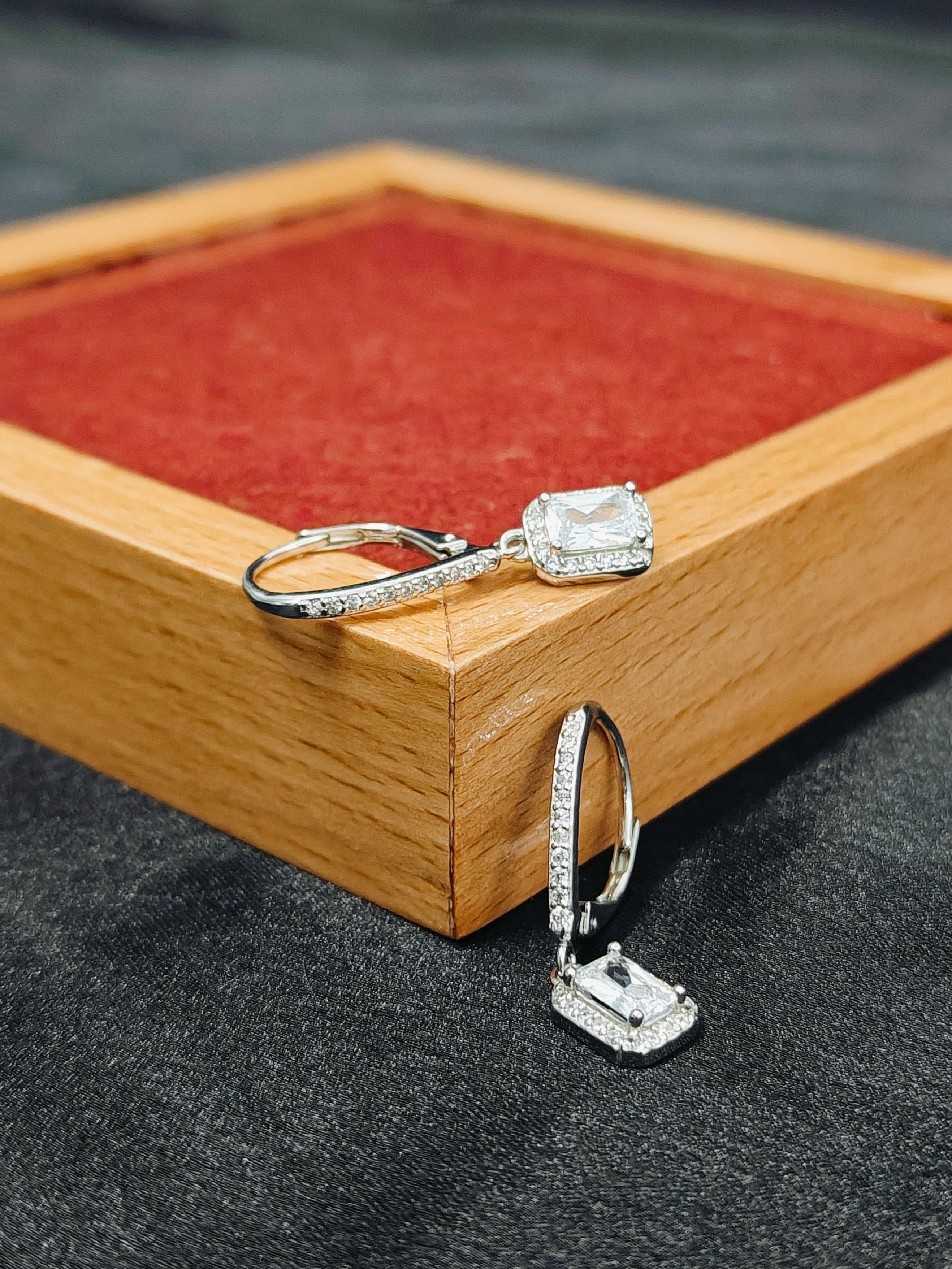 Silver earrings with gemstones on a wooden and red fabric background